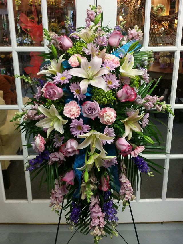 Standing floral spray with lilies, roses, and purple blooms on an easel