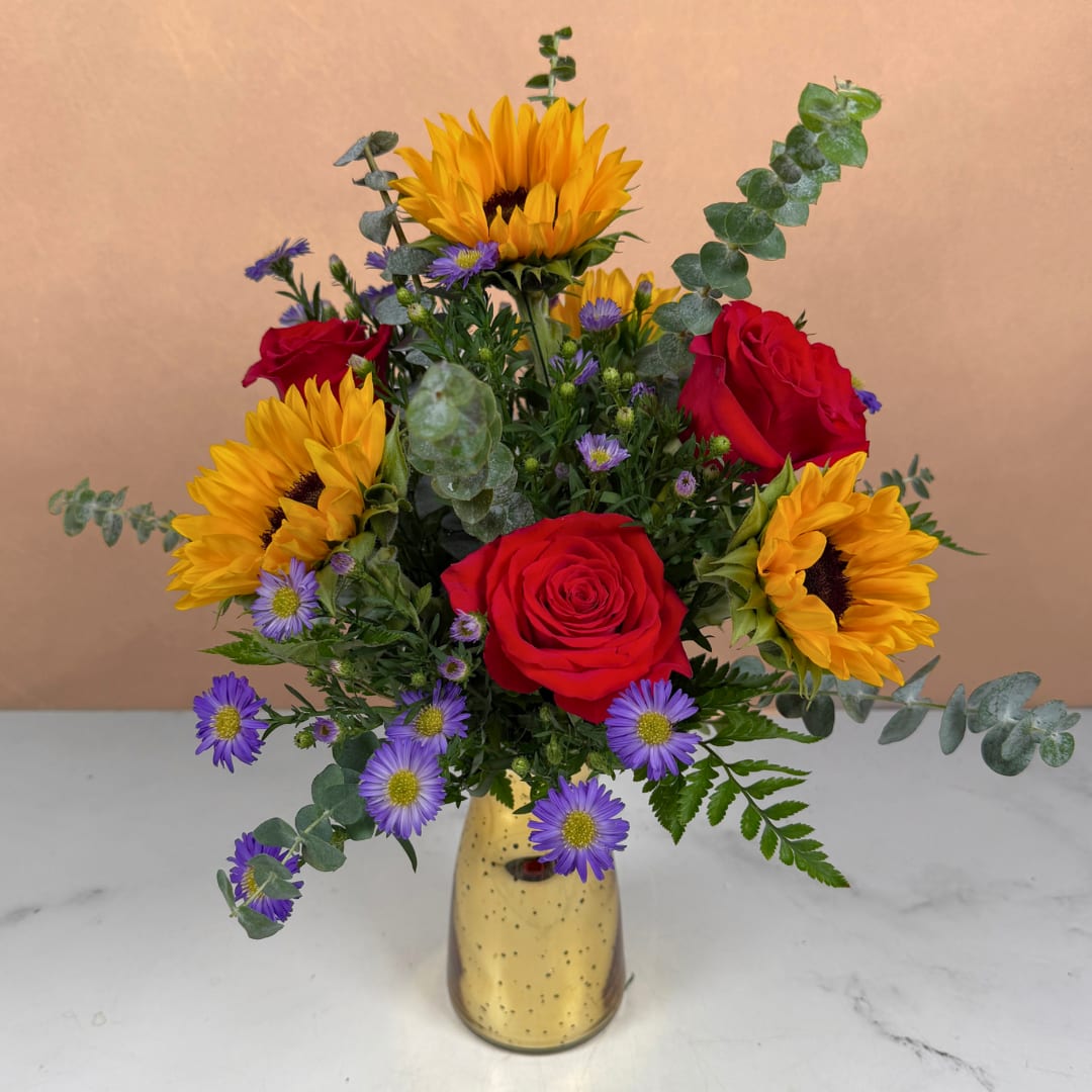 Bouquet of red roses, sunflowers, and purple daisies in a gold vase