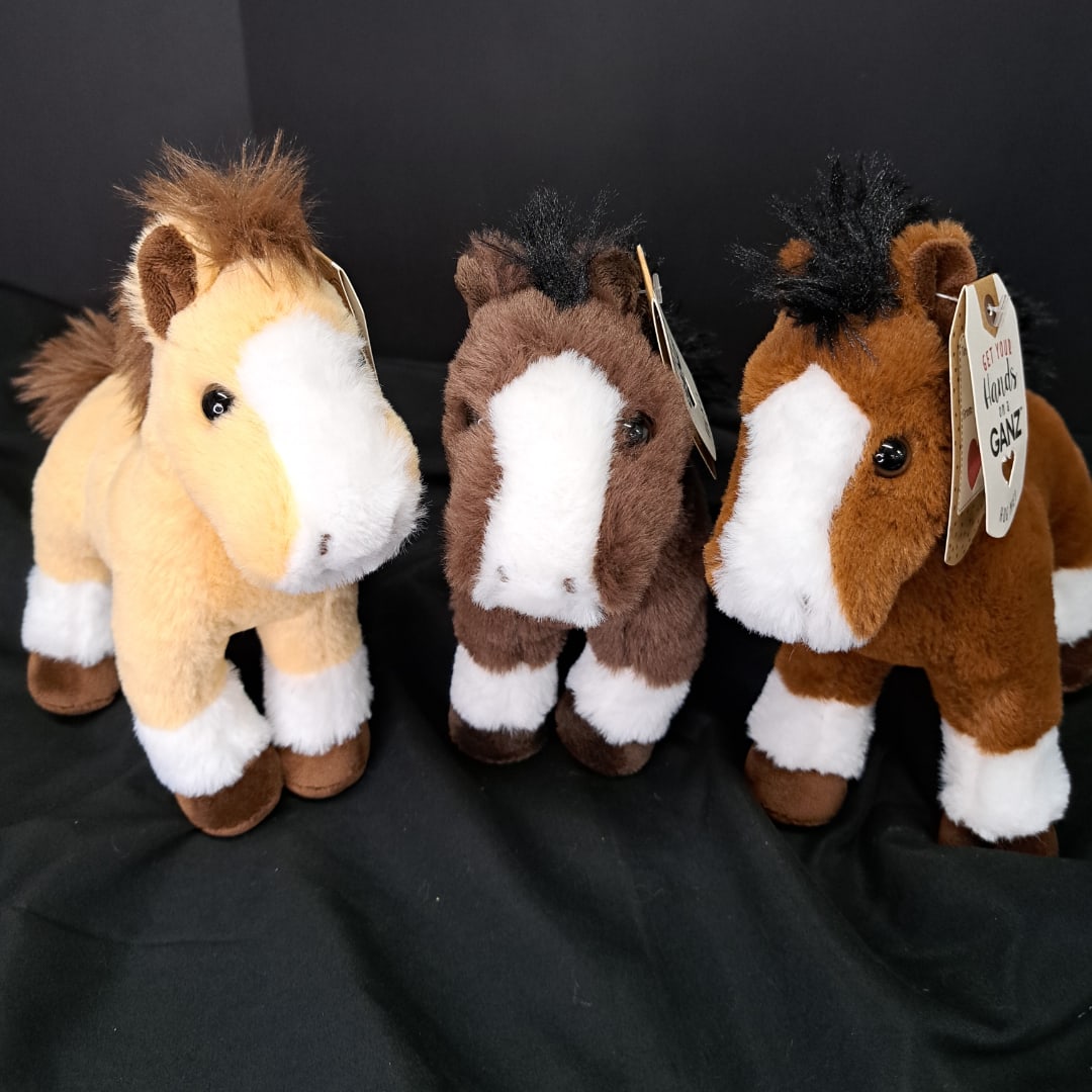 Three plush horse toys on a black fabric background
