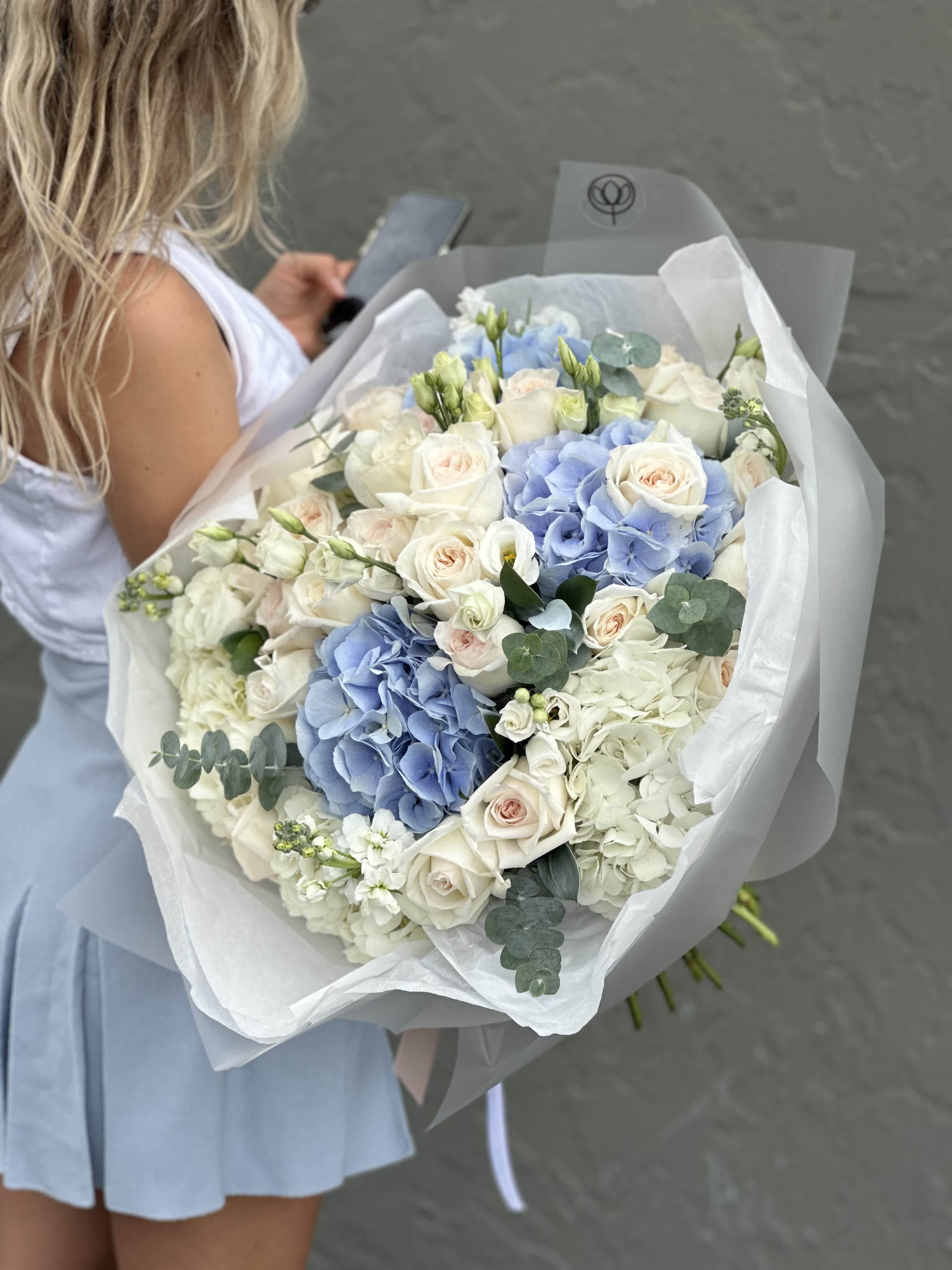 Large bouquet of white roses and blue hydrangeas wrapped in white paper