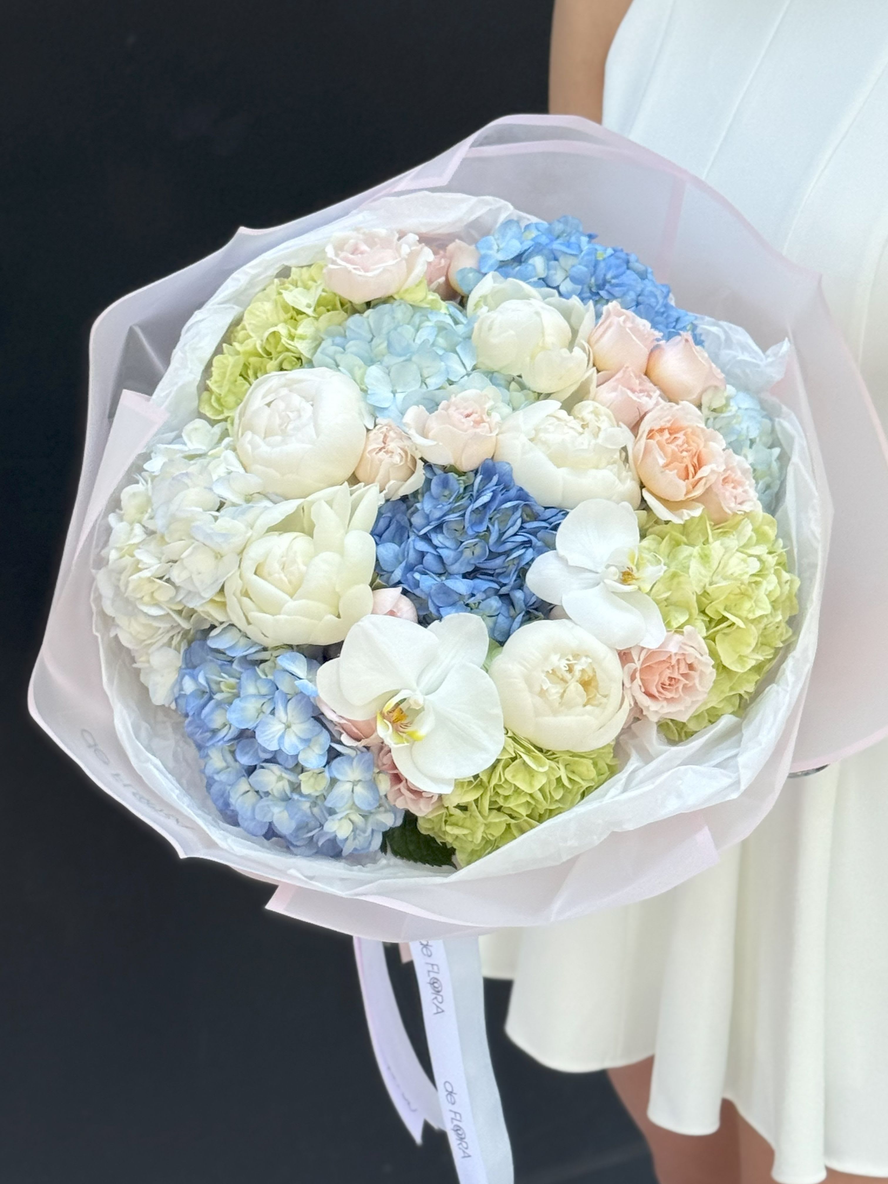 Pastel bouquet of hydrangeas, roses, and white orchids wrapped in pink paper