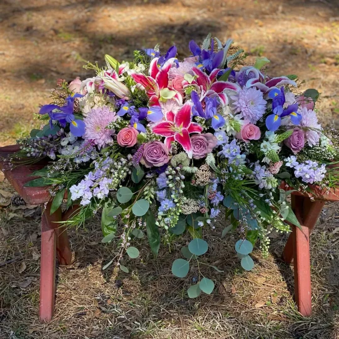 Large floral arrangement with pink lilies, roses, and purple blooms on a bench