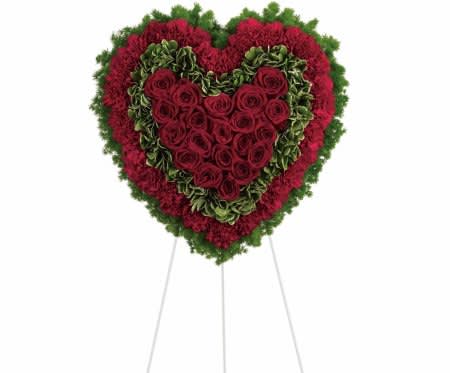 Heart-shaped standing floral arrangement of red roses and green flowers on a white easel