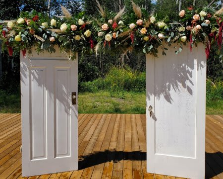 Tall rustic doorway arch made of two white doors topped with a garland of roses and grasses