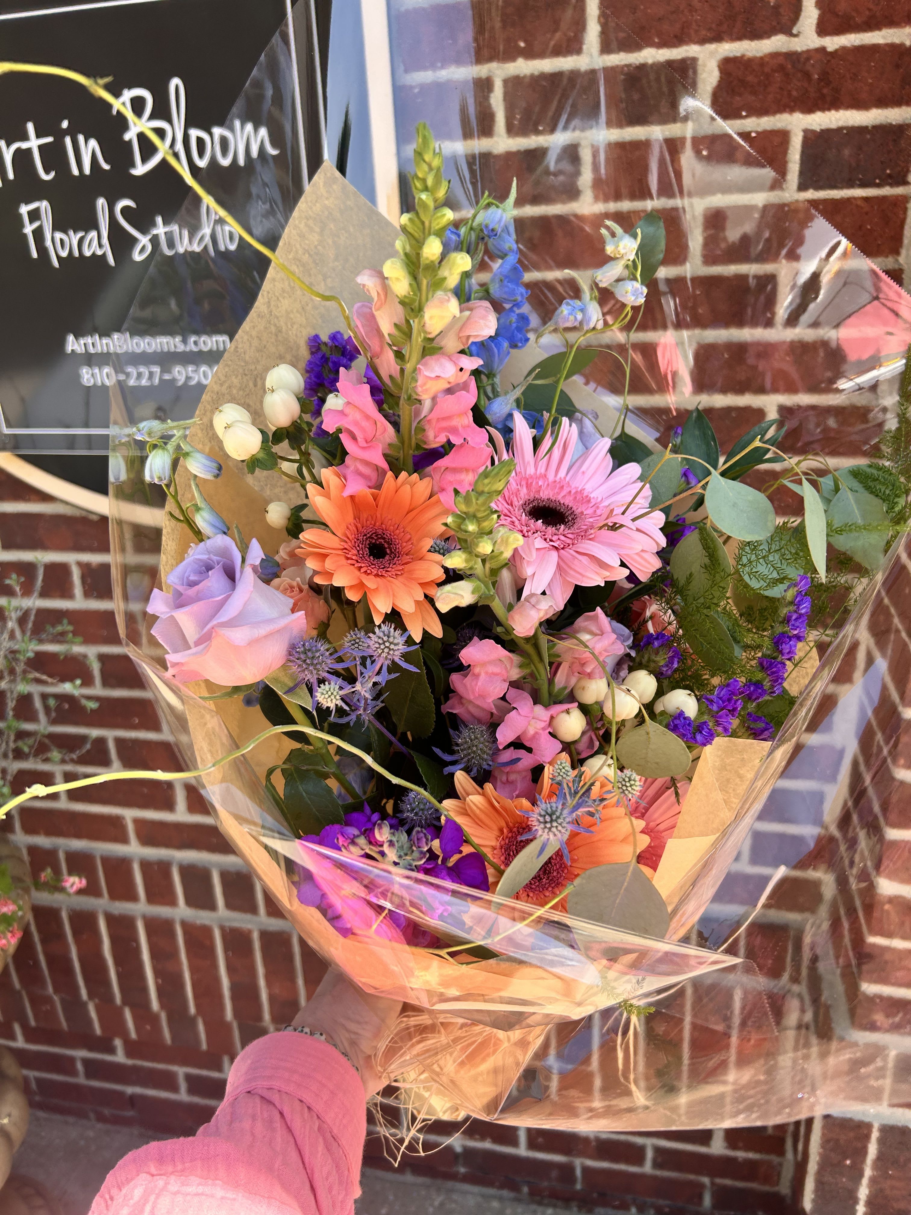 Colorful mixed bouquet with gerbera daisies, roses, and snapdragons in clear wrap