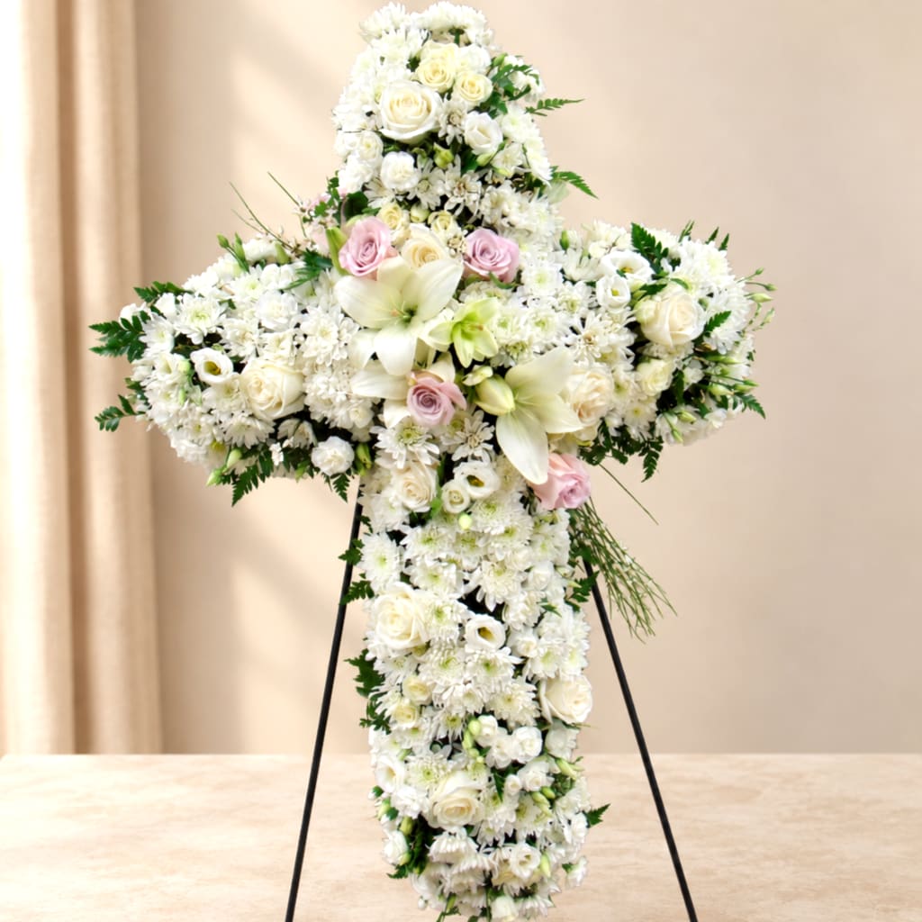 White floral cross arrangement on a stand with pale pink roses