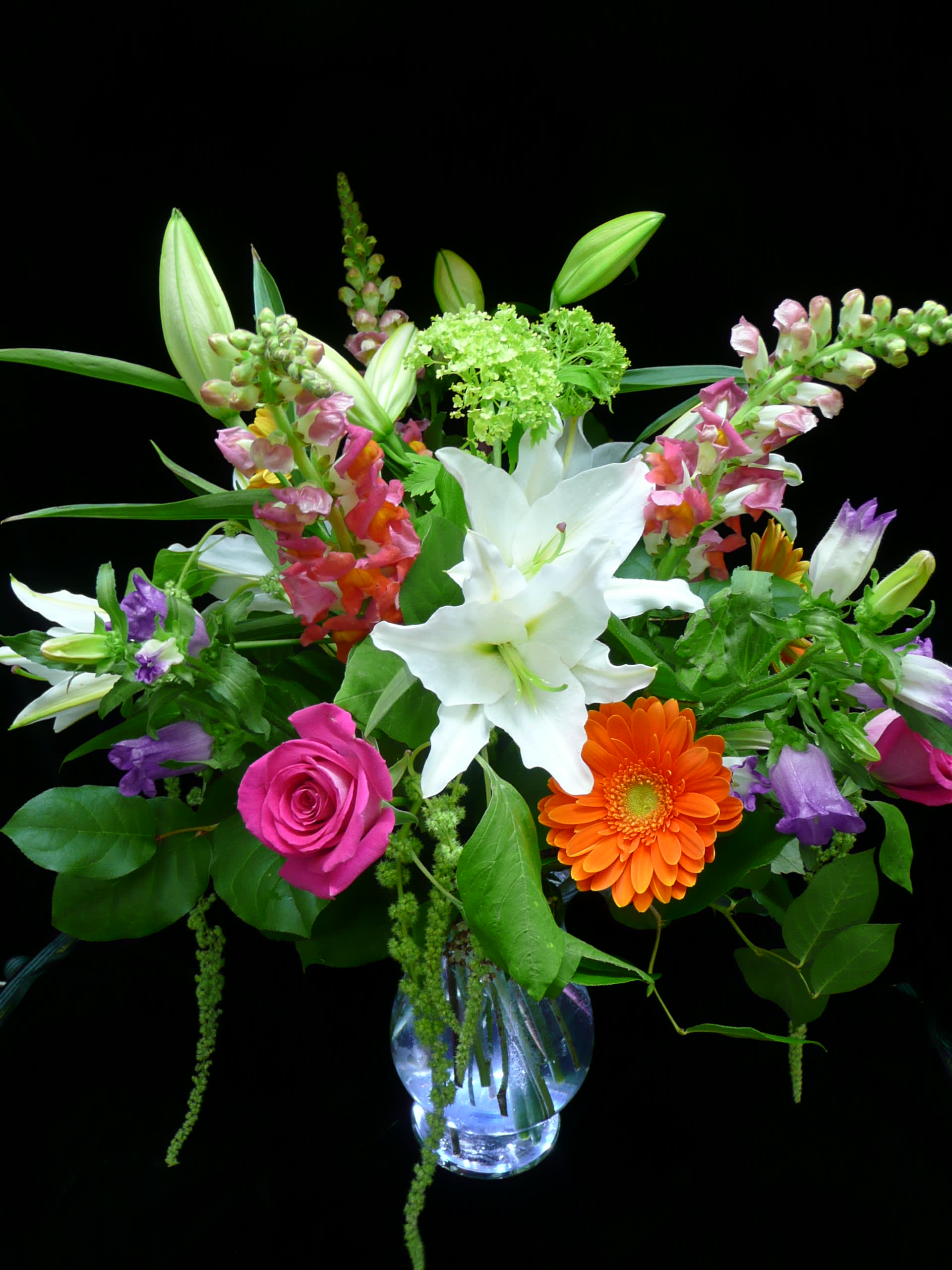 Mixed bouquet of white lilies, pink roses, and orange gerbera in a clear glass vase.