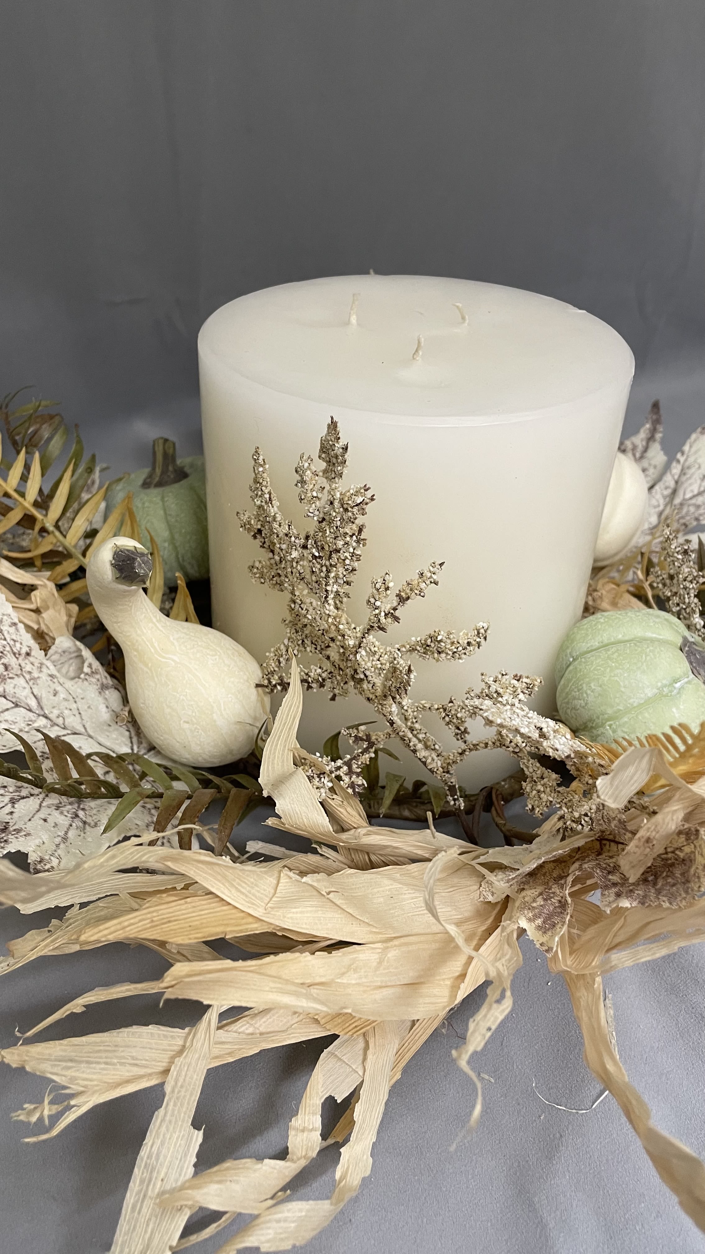 Large white pillar candle surrounded by dried foliage and decorative gourds