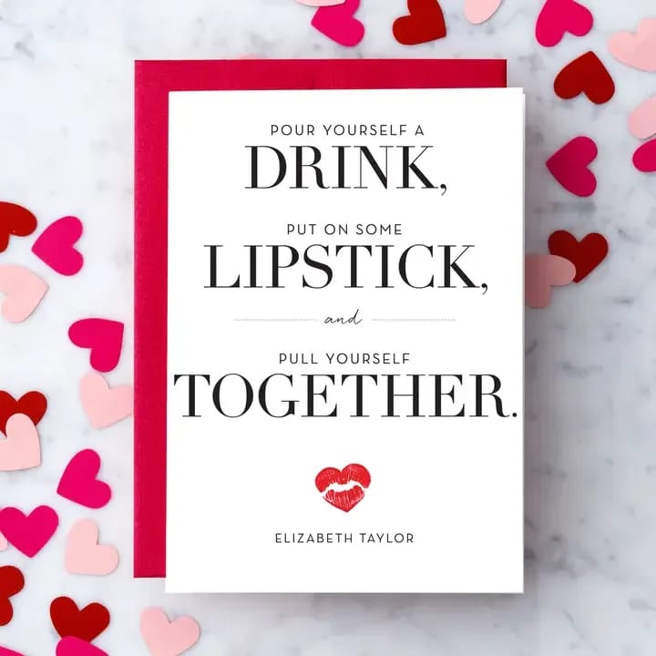White greeting card with bold black text and red lipstick print, on red envelope with scattered paper hearts.
