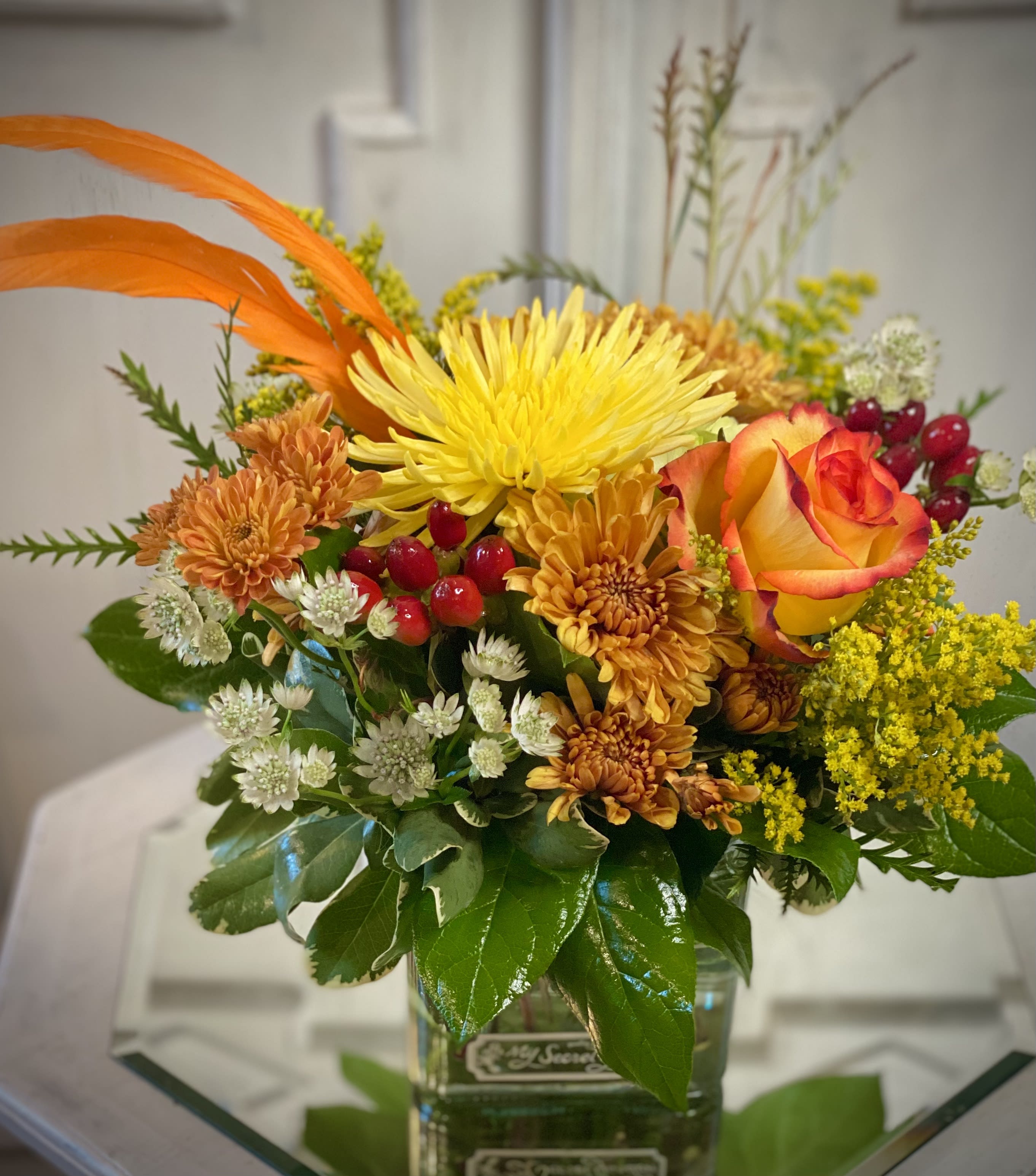 Orange and yellow floral arrangement in a glass vase with a rose and chrysanthemums