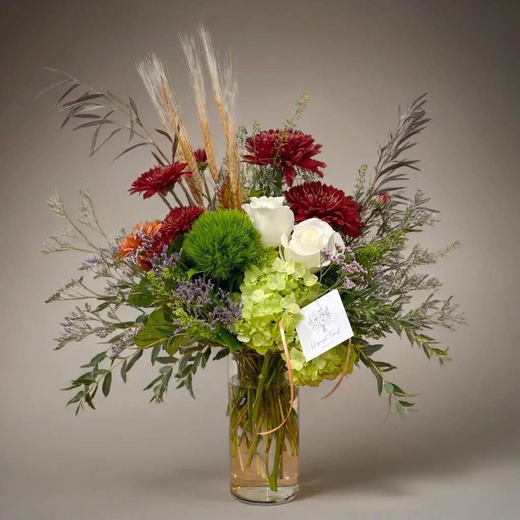 Autumn Fields - Bring refined fall elegance into your home with our Autumn Fields Vase Arrangement, a tall Thanksgiving flower design inspired by natural harvest textures and soft seasonal colors. This airy, organic bouquet features rich burgundy mums, bright green trick dianthus, soft white roses, fresh green hydrangea, lavender filler, and wispy fall greenery. Wheat stems add height and a rustic harvest touch, creating a beautiful blend of farmhouse charm and modern style.  Perfect for Thanksgiving celebrations, fall gatherings, entryway décor, or as a thoughtful seasonal gift, this arrangement offers a lighter, more sophisticated take on traditional autumn flowers. If you’re searching for tall fall arrangements, Thanksgiving flowers, or a rustic autumn vase bouquet, this design brings graceful movement and natural beauty to any space.  Approximately 16"w x 21"h  Available for delivery to the Quad Cities and surrounding area.
