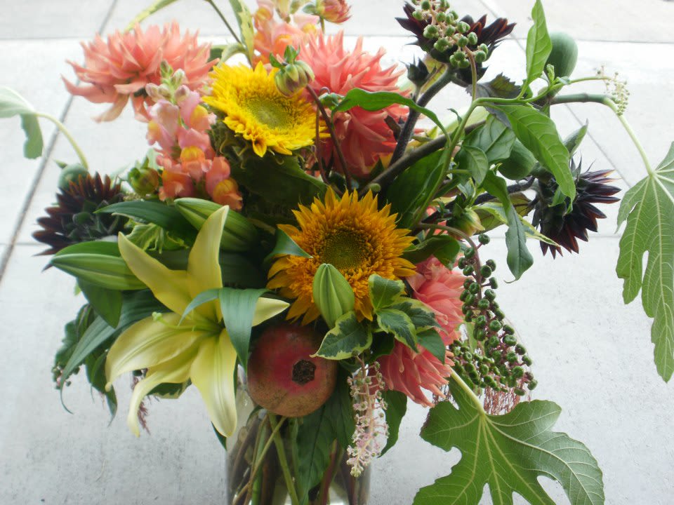 Loose garden-style bouquet with yellow sunflowers, peach dahlias, and lilies in a clear glass vase
