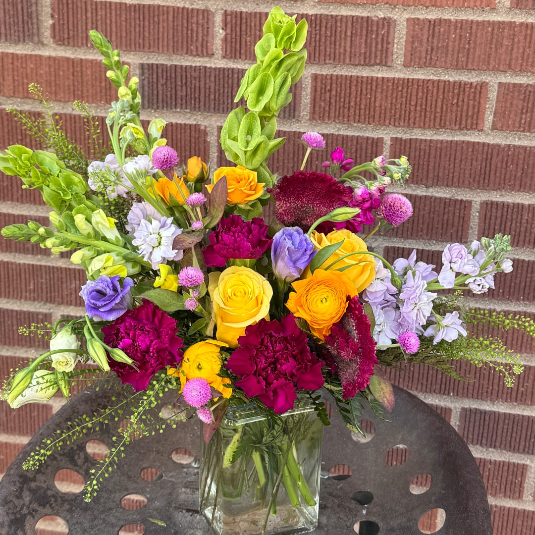 Mixed bouquet in a clear glass vase with yellow, purple, pink, and white blooms