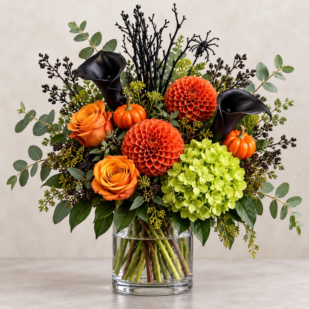 Orange and black floral arrangement in a clear glass vase with pumpkins