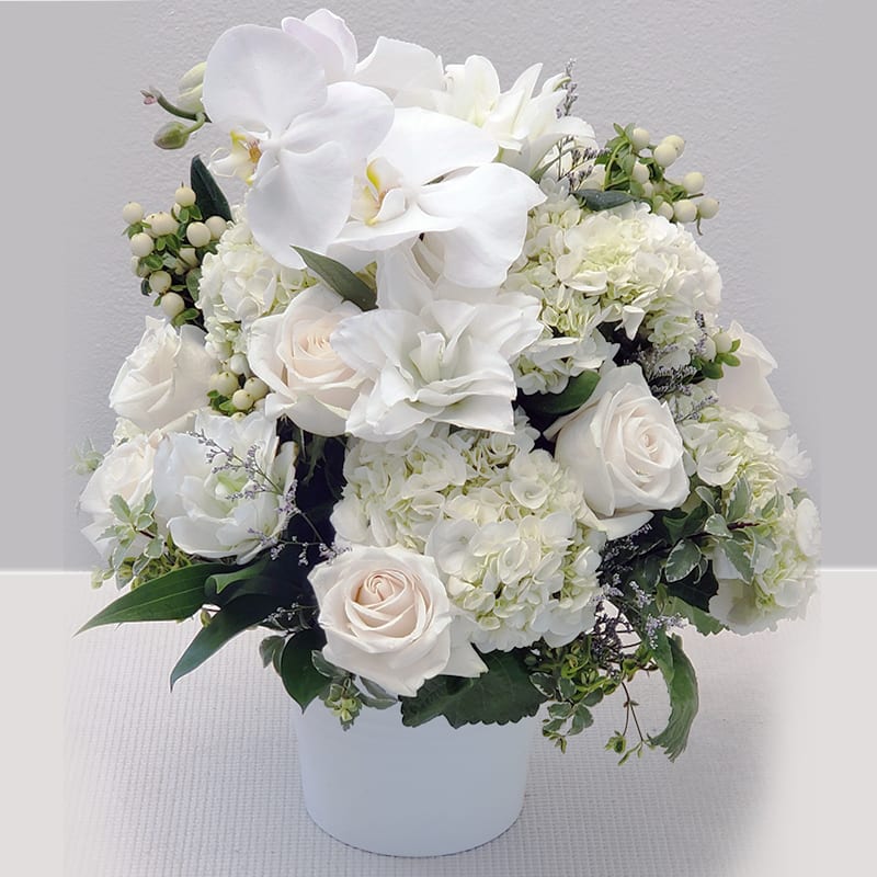 White roses and orchids arranged in a white vase