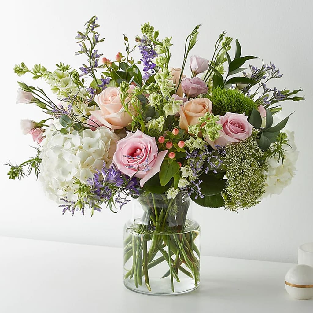Mixed pastel bouquet of roses, hydrangeas, and purple flowers in a glass vase