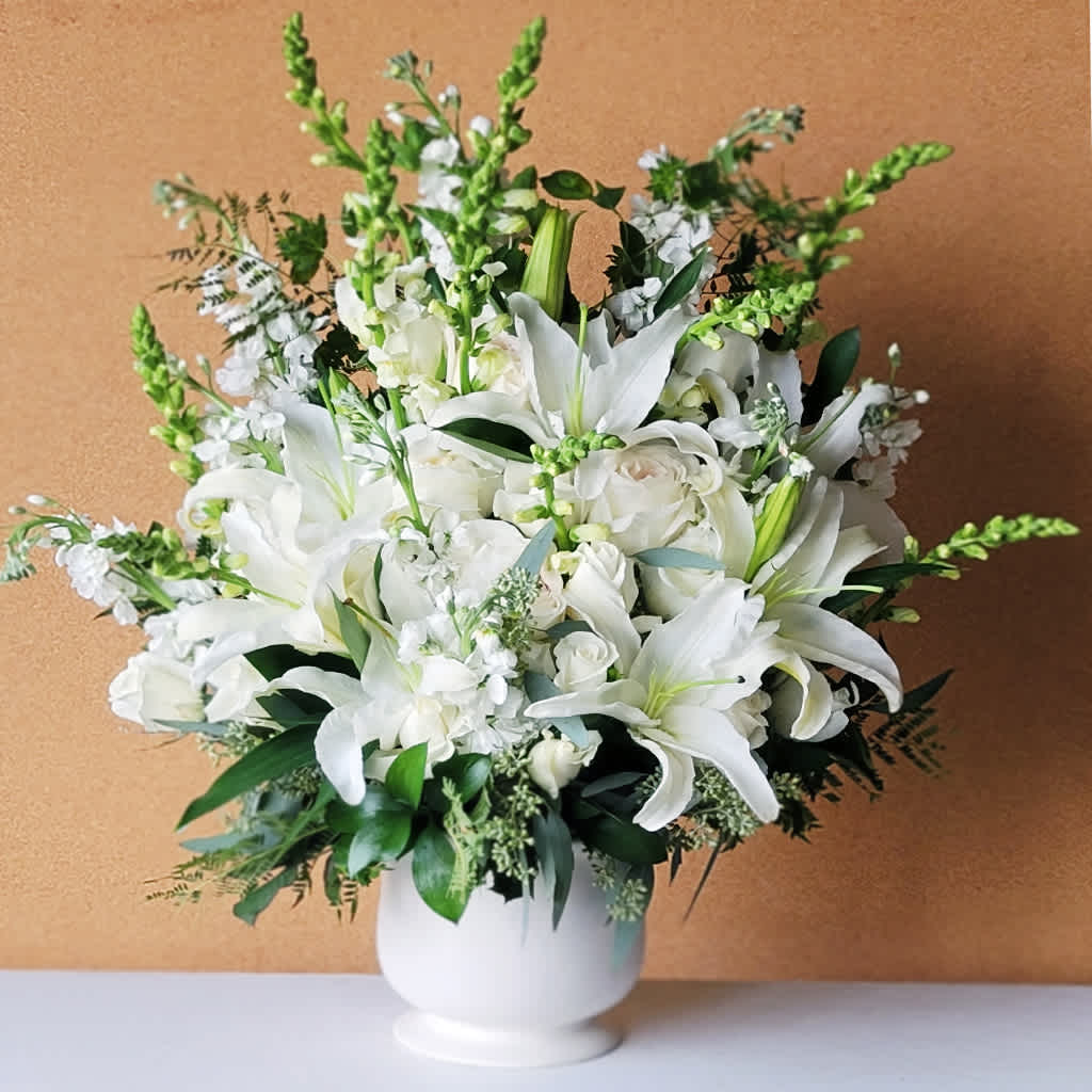 Sweet Comfort Spray Arrangement - Overflowing with a variety of white lilies, roses, snapdragons, stock, hydrangea, and greenery, it conveys a sense of peace that reaches outward with its serene beauty.  Ideal for expressing sympathy, sending condolences, or honoring a loved one at a funeral or memorial service.