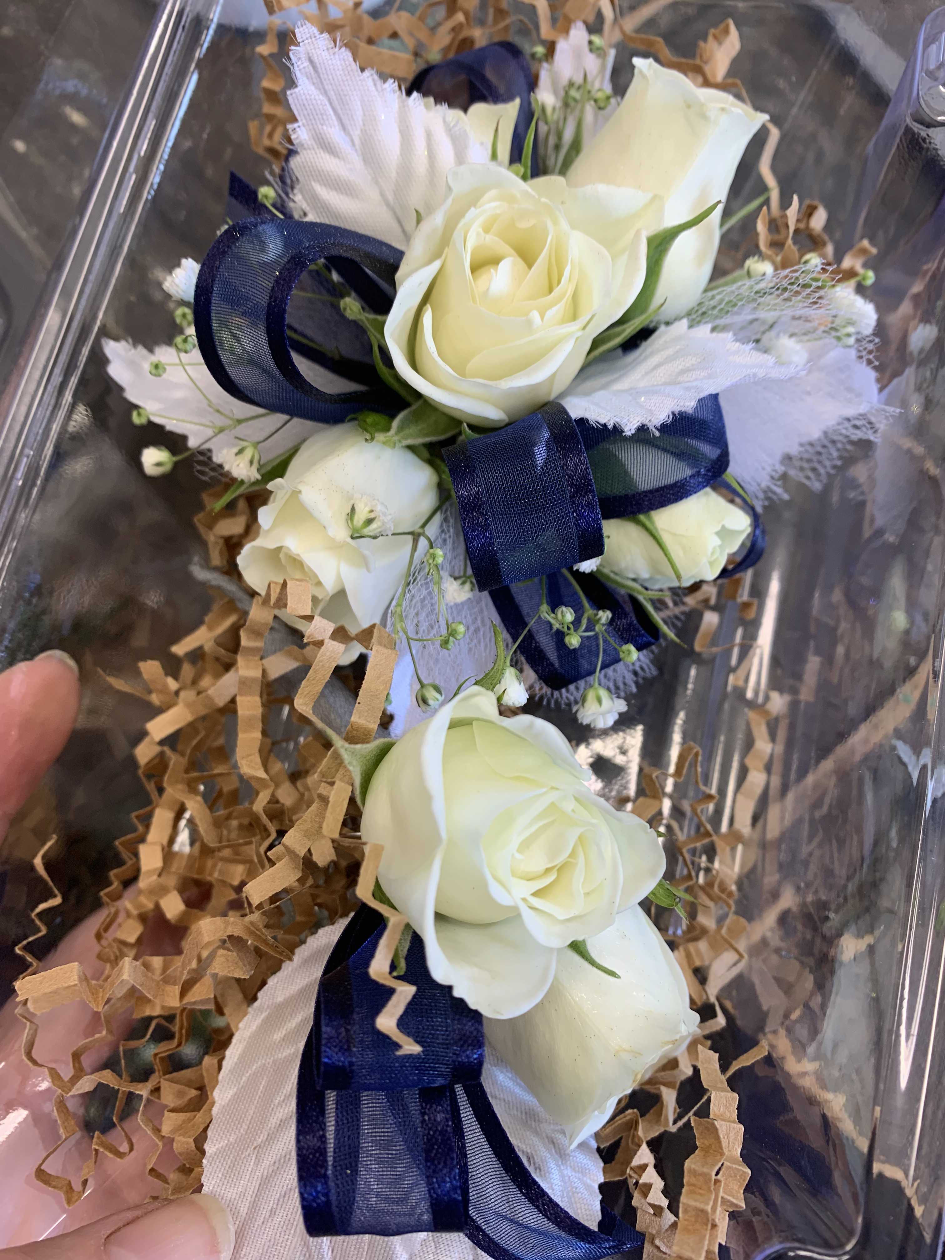 White rose corsage with navy ribbon in clear packaging