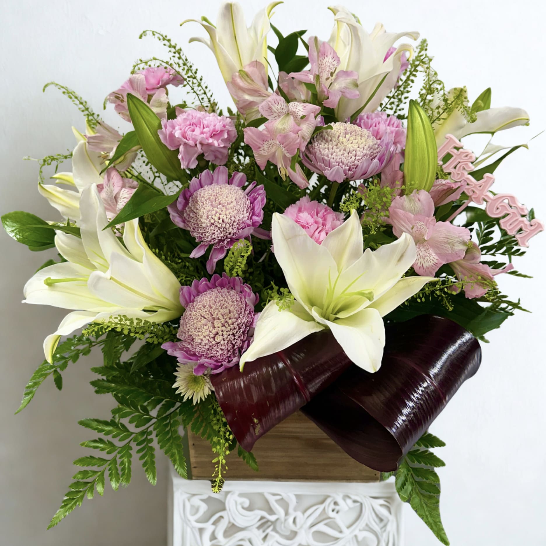 Pink and white floral arrangement in a wooden box with burgundy ribbon