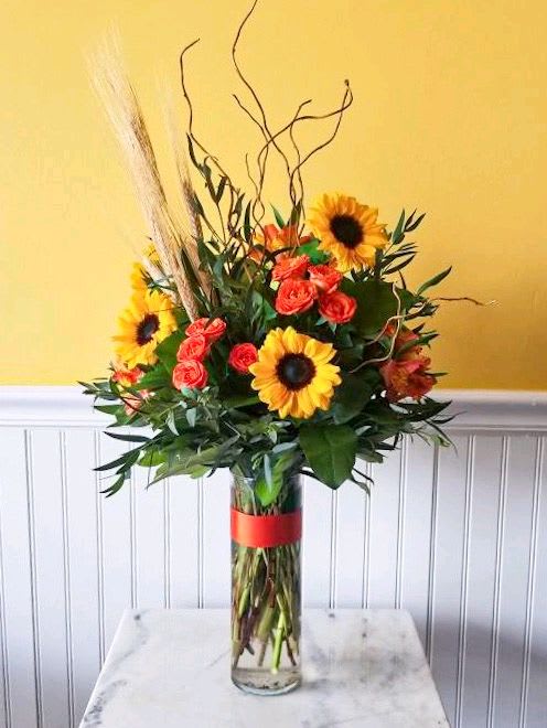 Sunflower and rose arrangement in a tall glass vase with a red ribbon