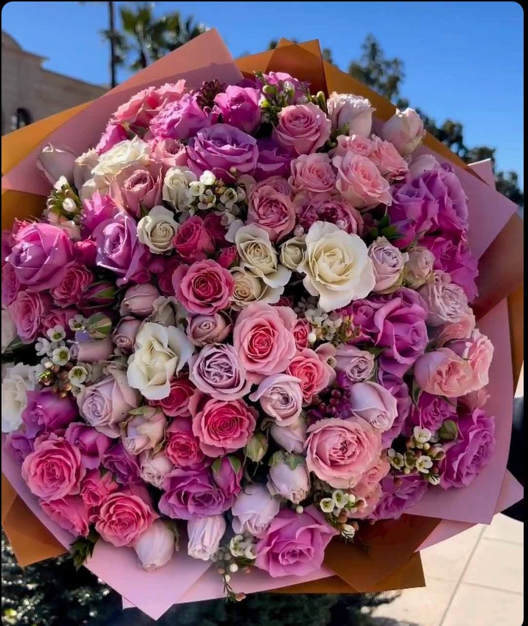 Large bouquet of pink, purple, and white roses wrapped in pastel paper