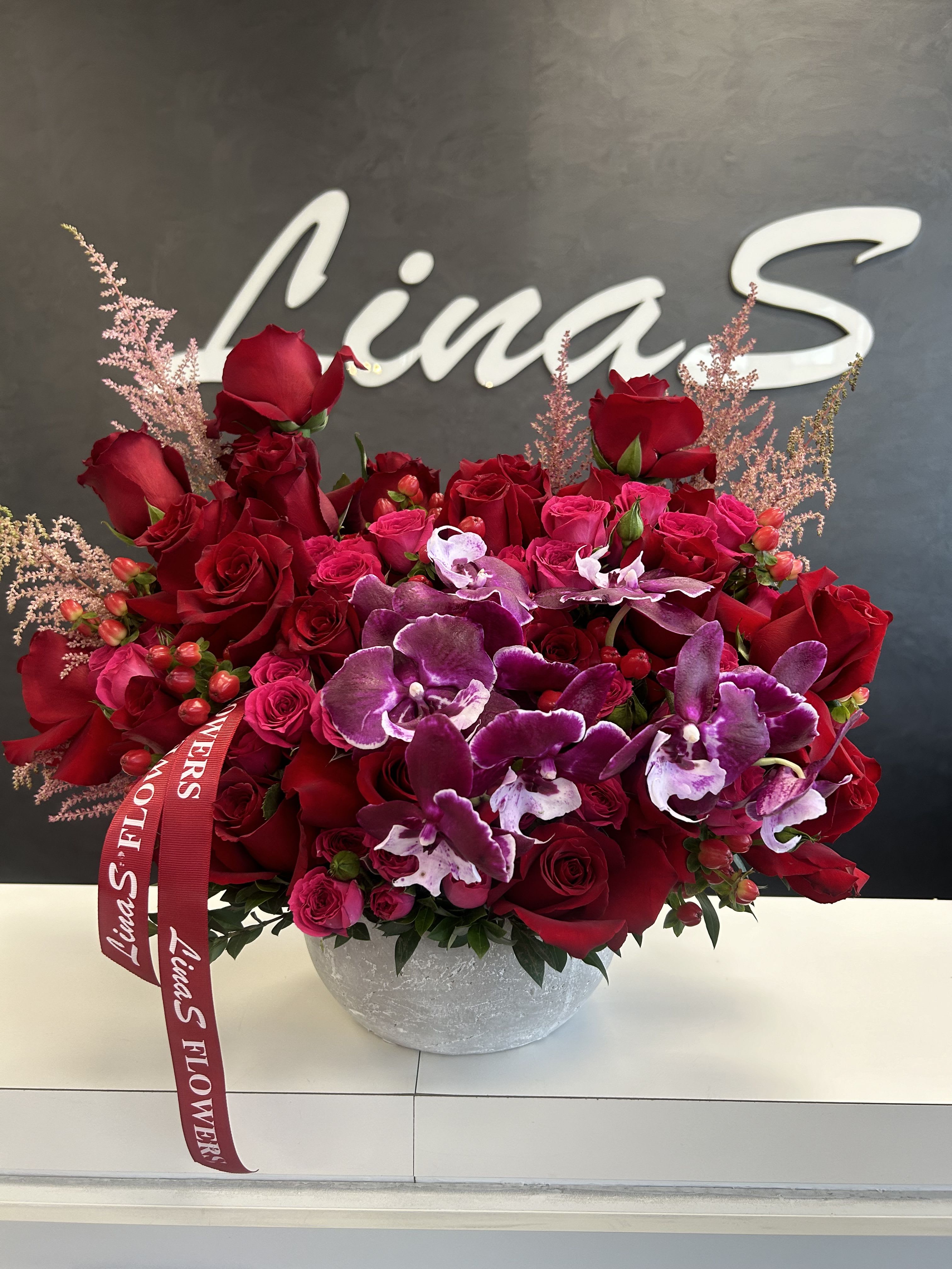 Red roses and purple orchids in a round gray vase with a ribbon