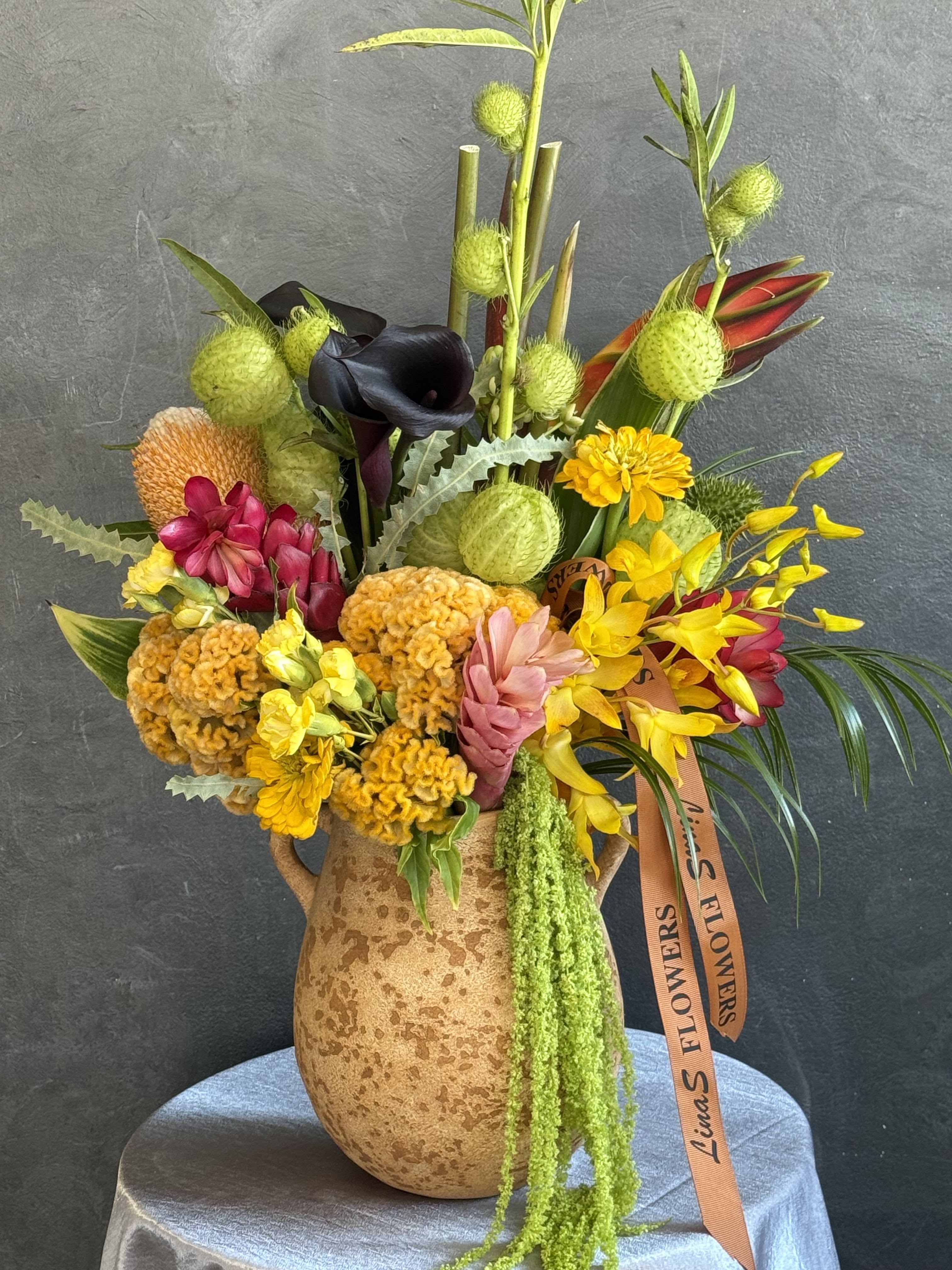 Mixed tropical bouquet in a speckled ceramic vase with bright yellow and pink blooms