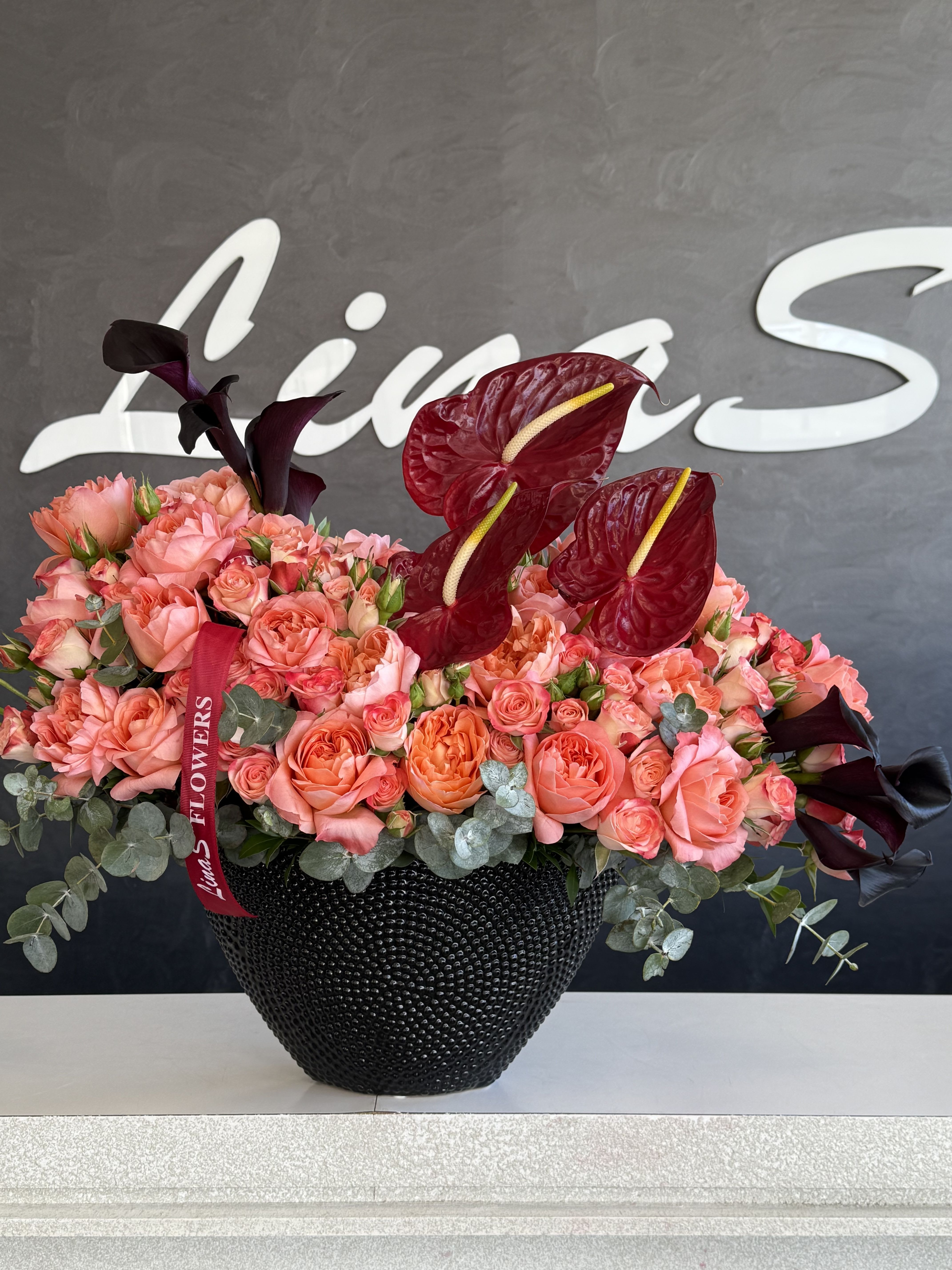 Pink and coral roses in a black vase with dark red anthuriums