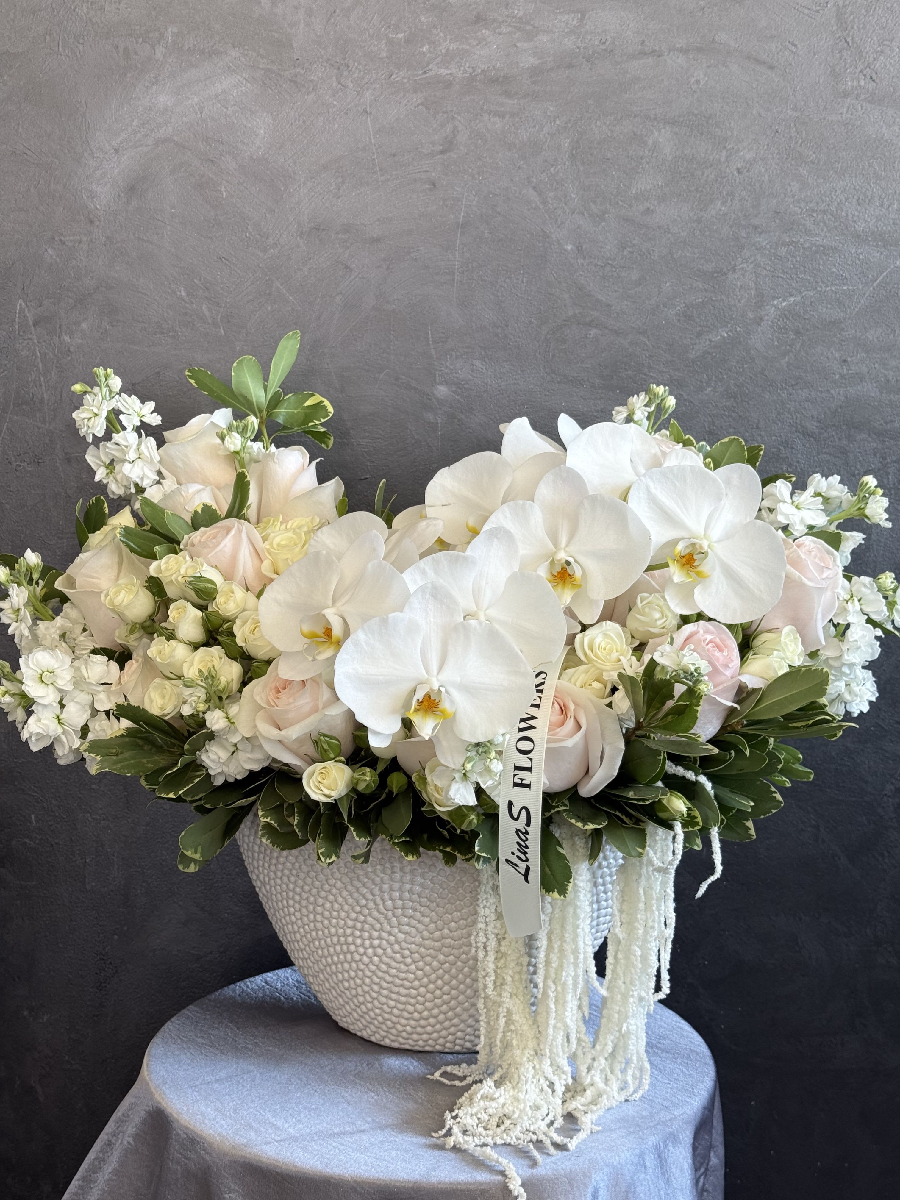 White orchids and pale roses in a textured vase with trailing white strands