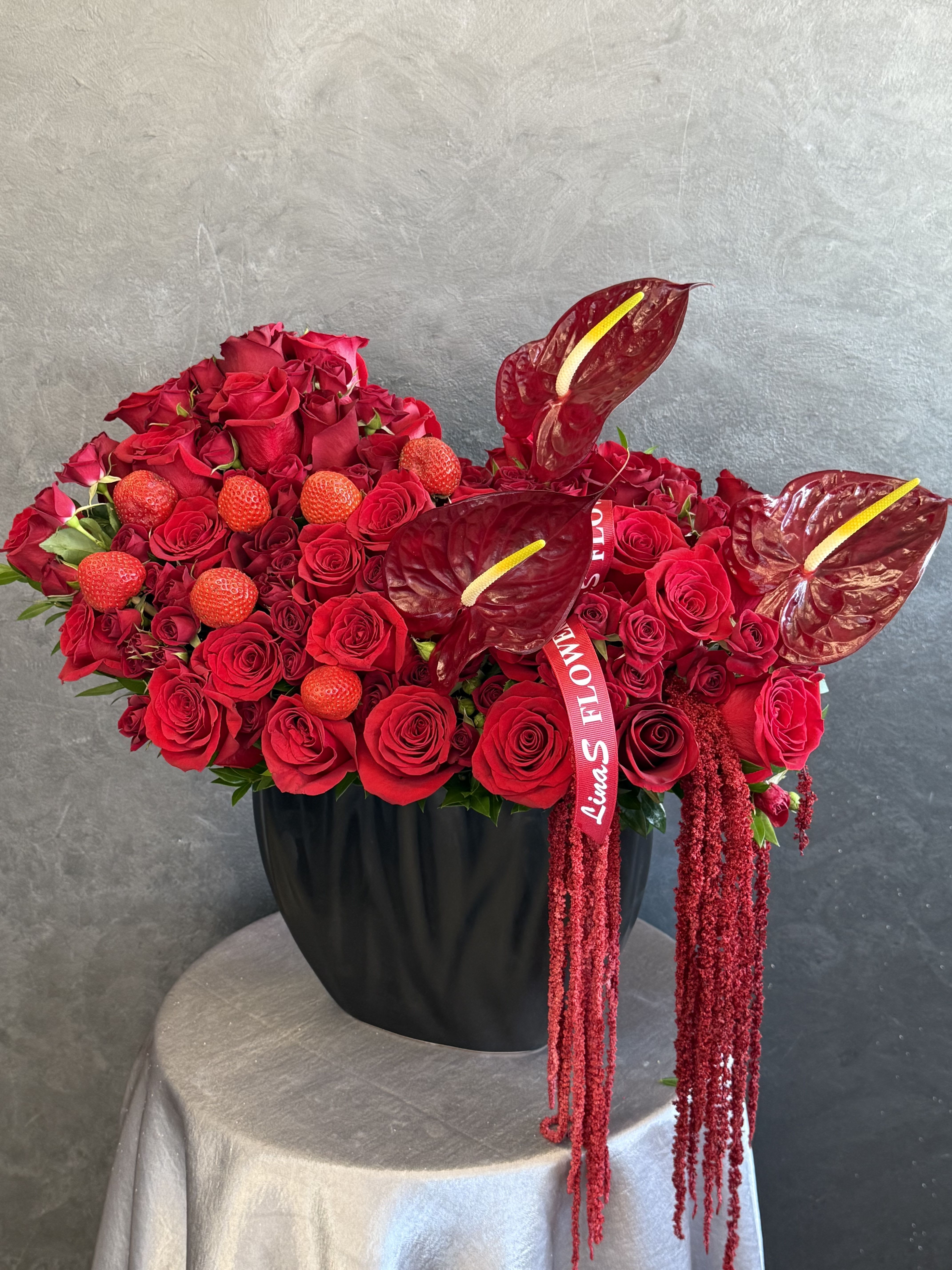 Red rose arrangement in a black vase with anthuriums and hanging red accents