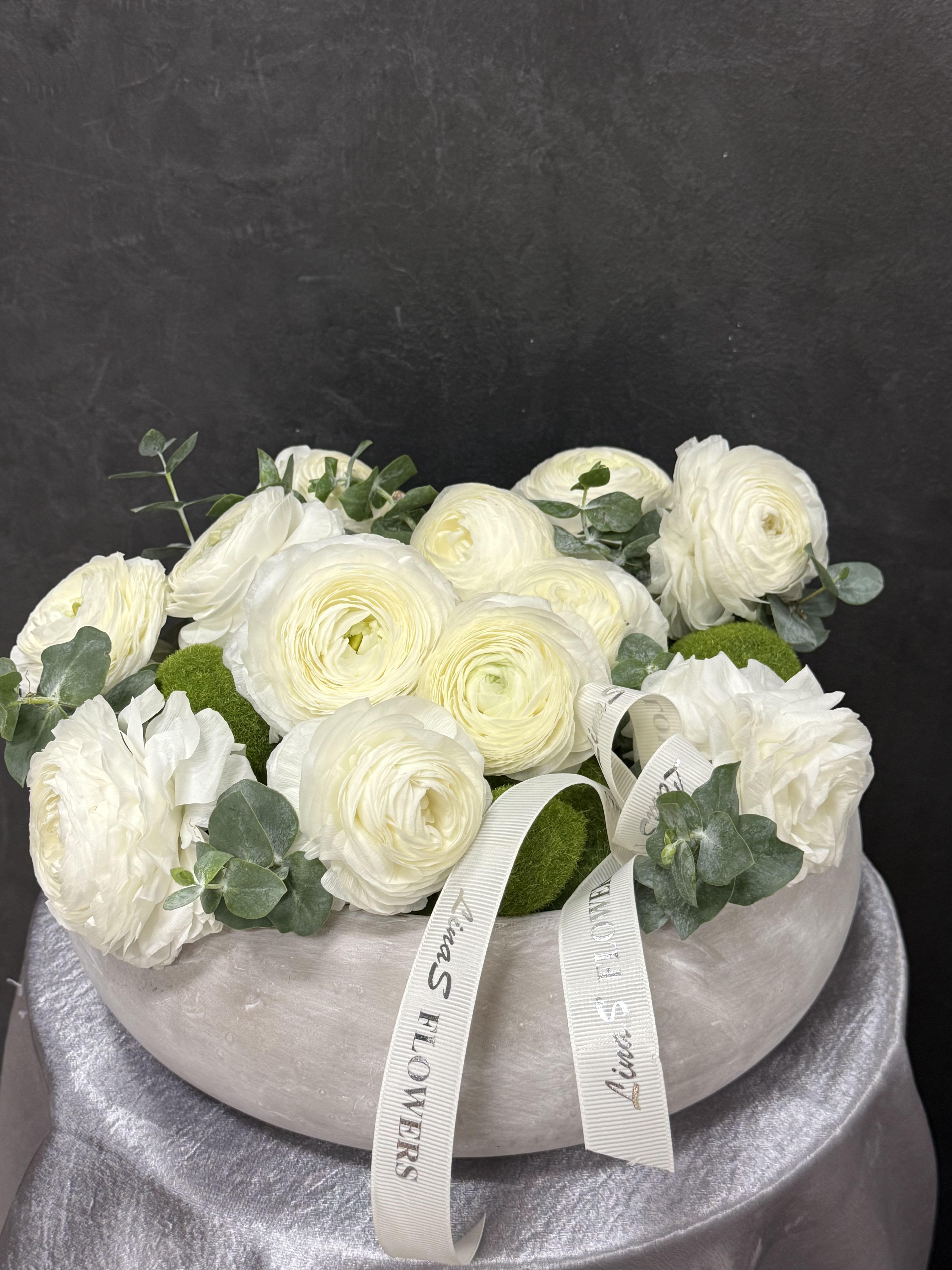 White ranunculus arrangement in a round vase with eucalyptus and ribbon