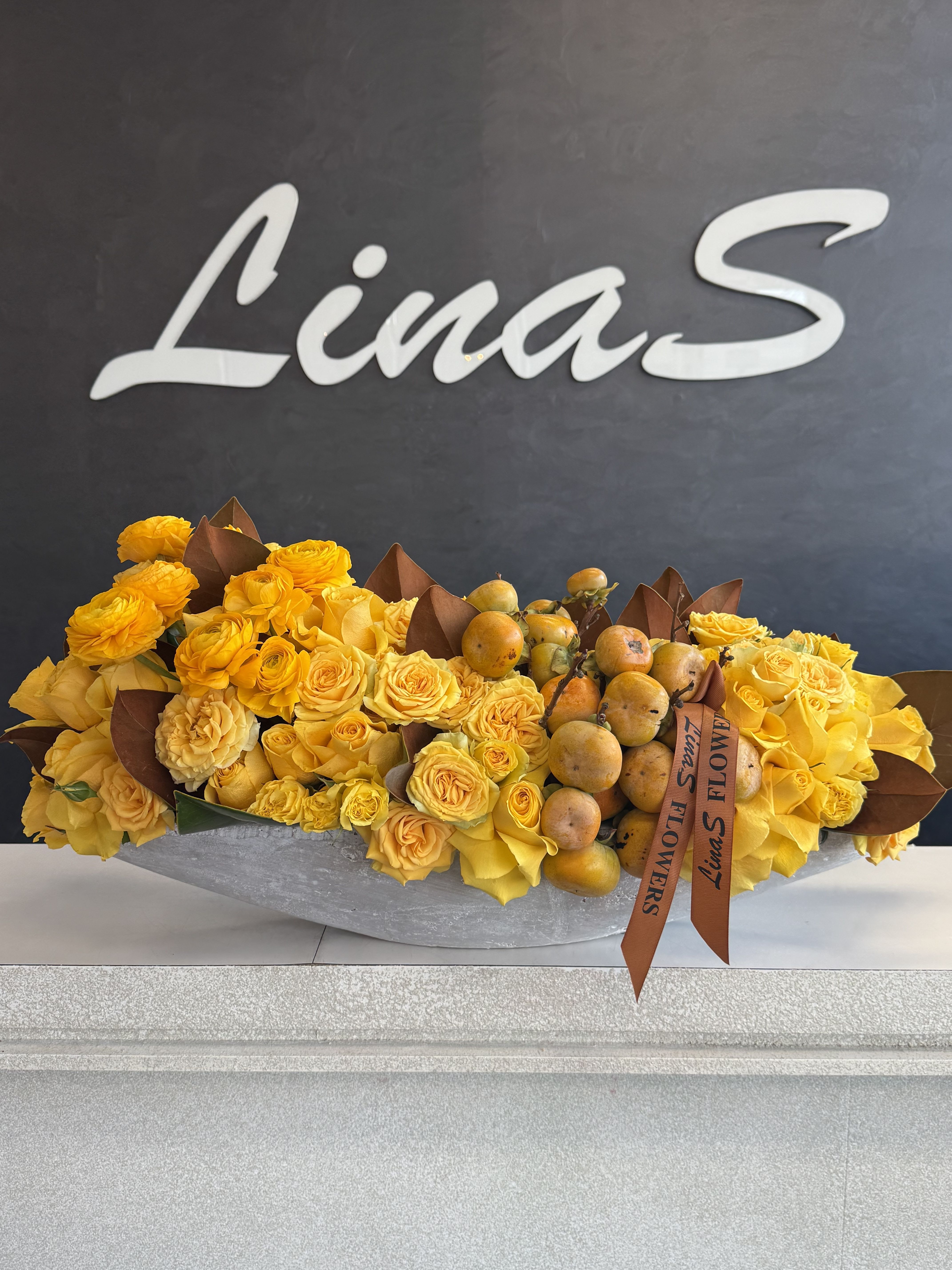 Yellow rose arrangement with fruit in a low gray container
