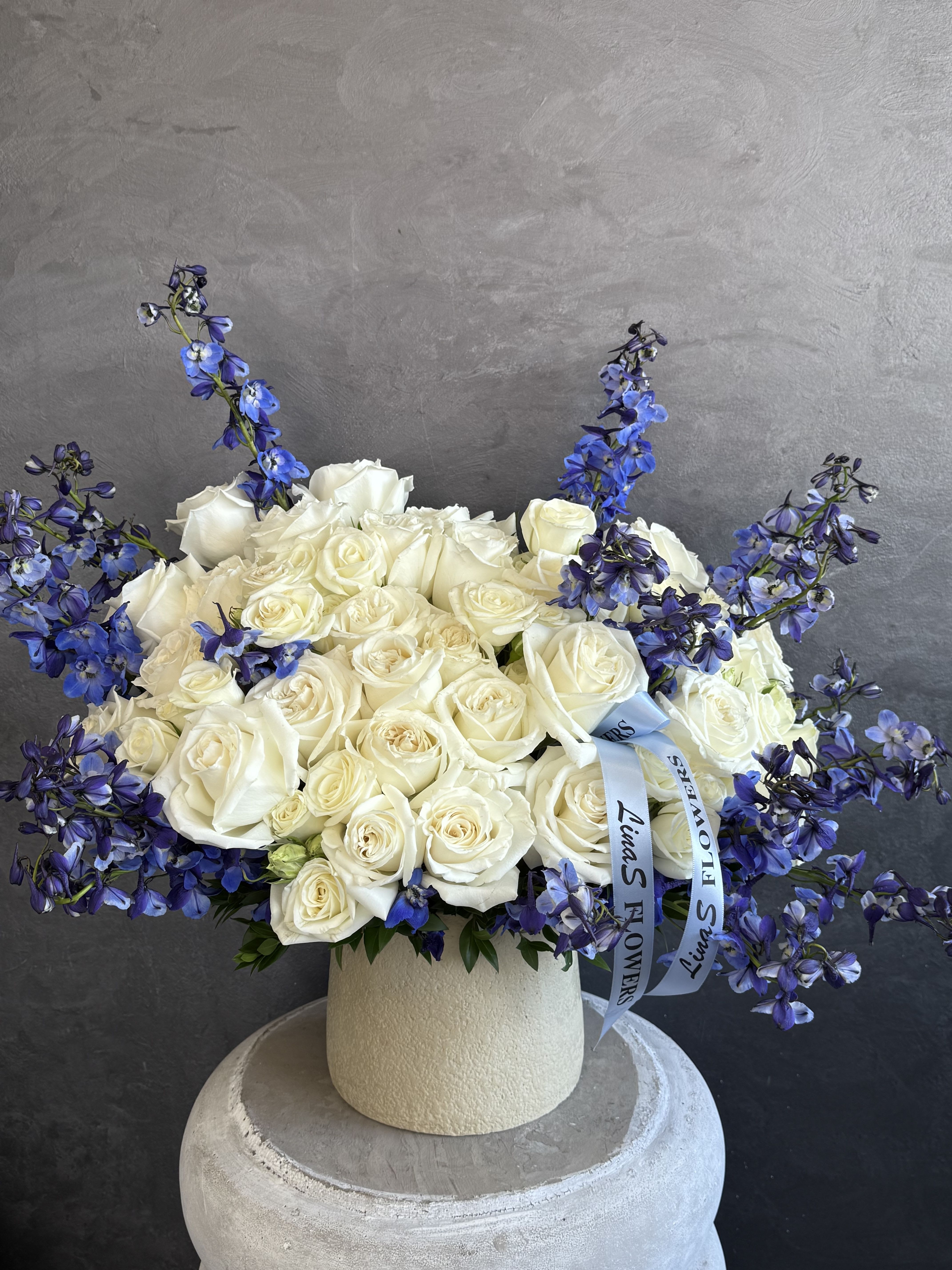 White rose arrangement with blue delphinium in a cream vase