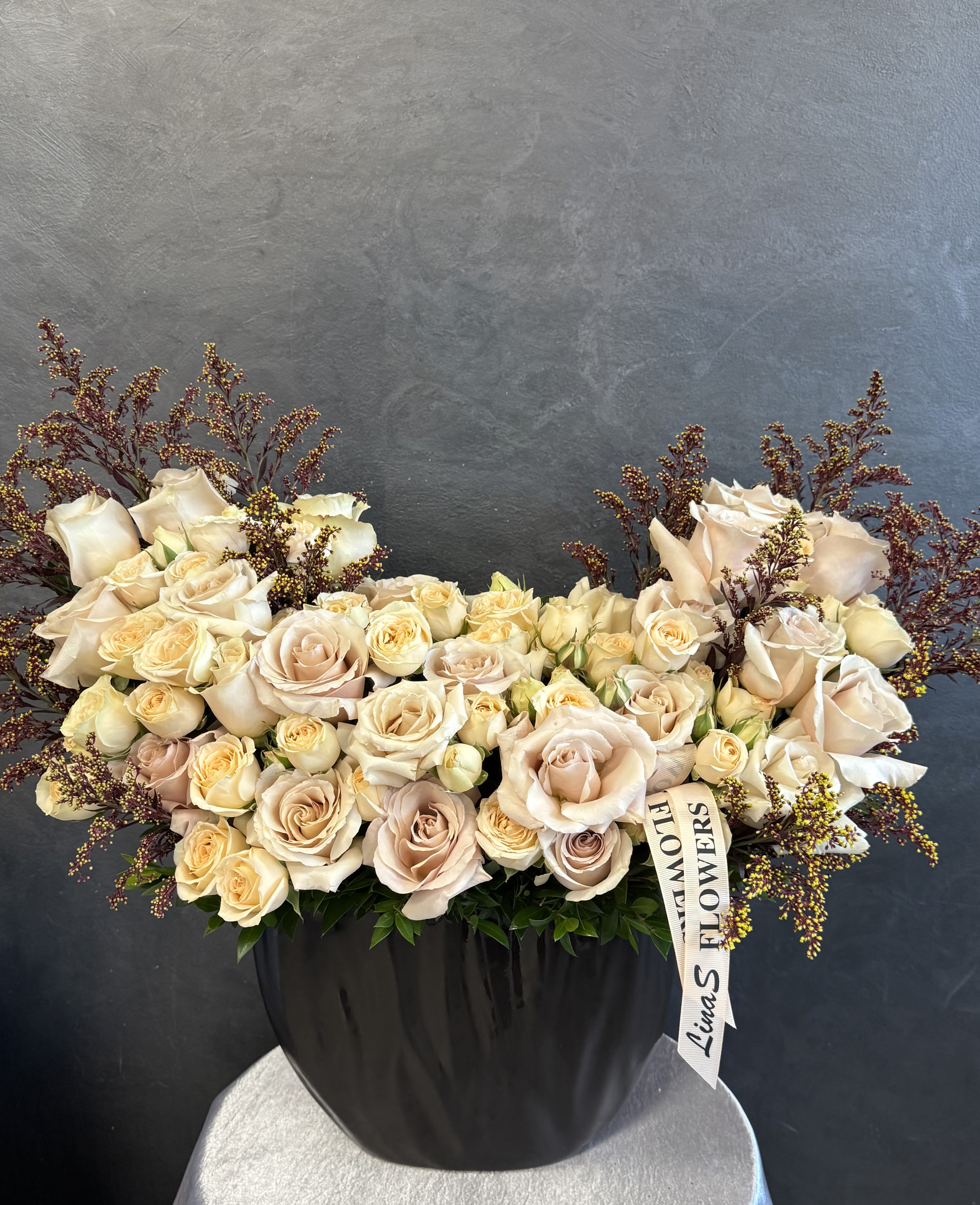 Large cream rose arrangement in a black vase with burgundy filler