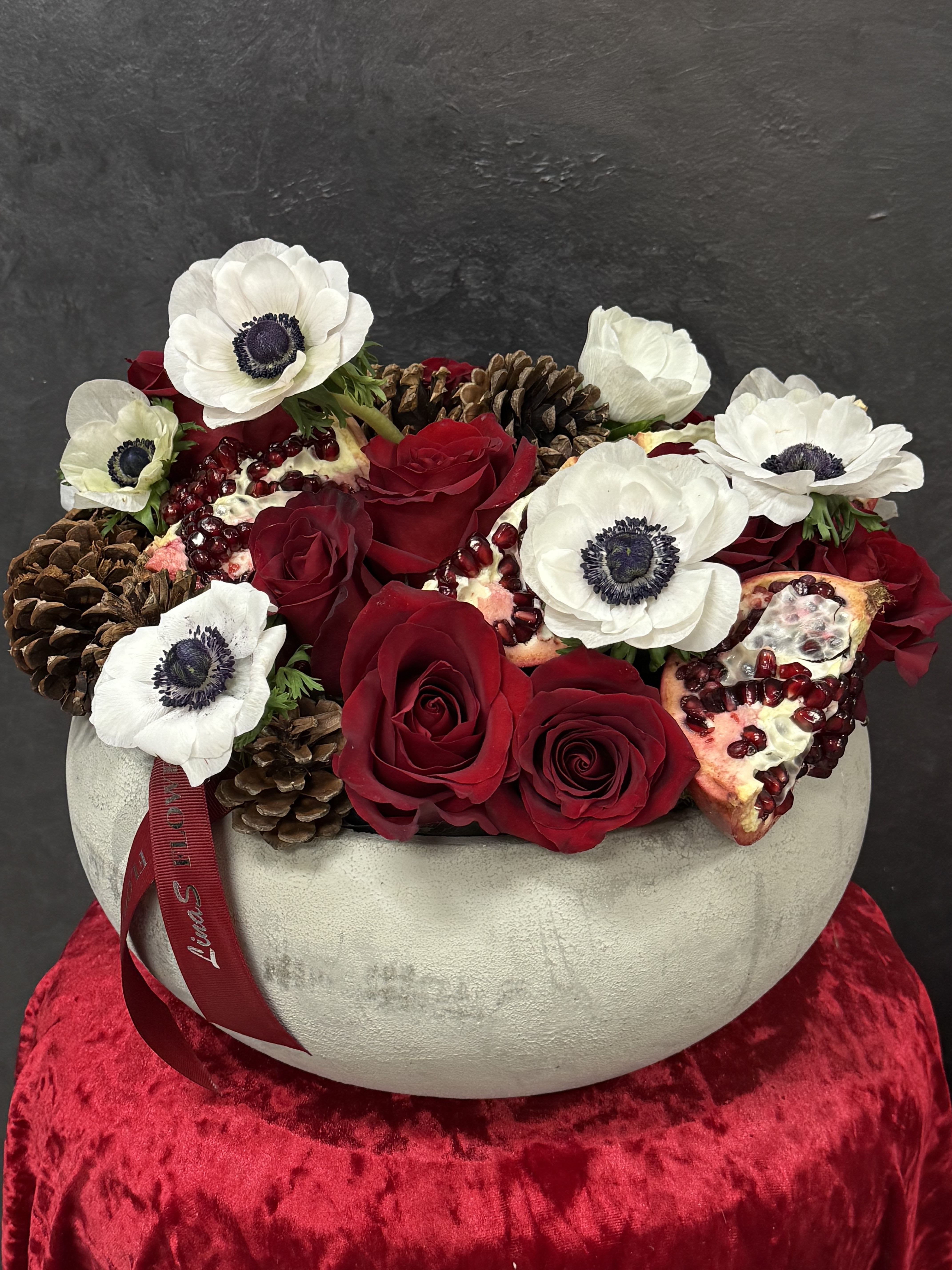 Red roses and white anemones in a round vase with pinecones and pomegranate pieces