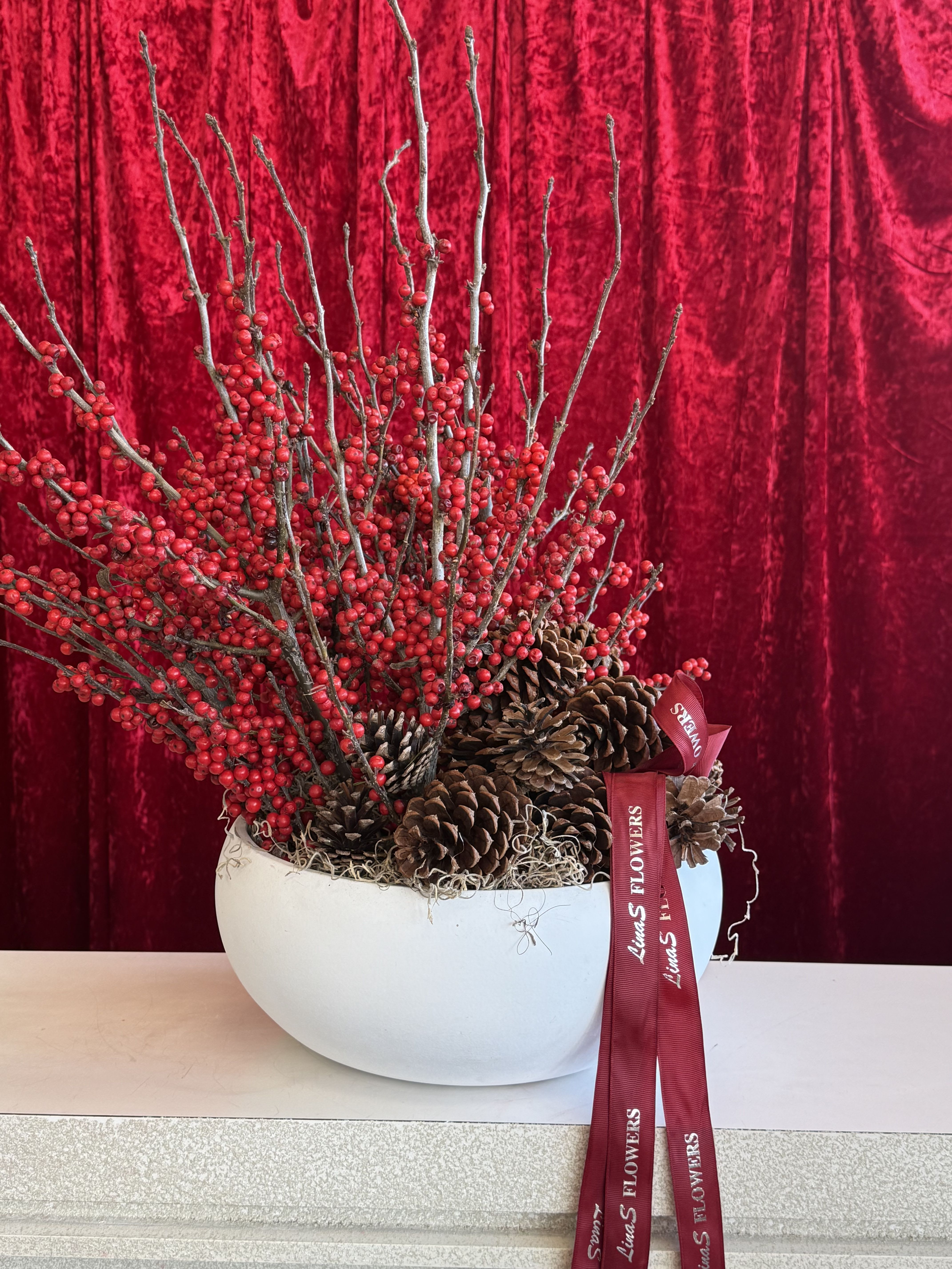 Red berry branches and pinecones in a white bowl vase