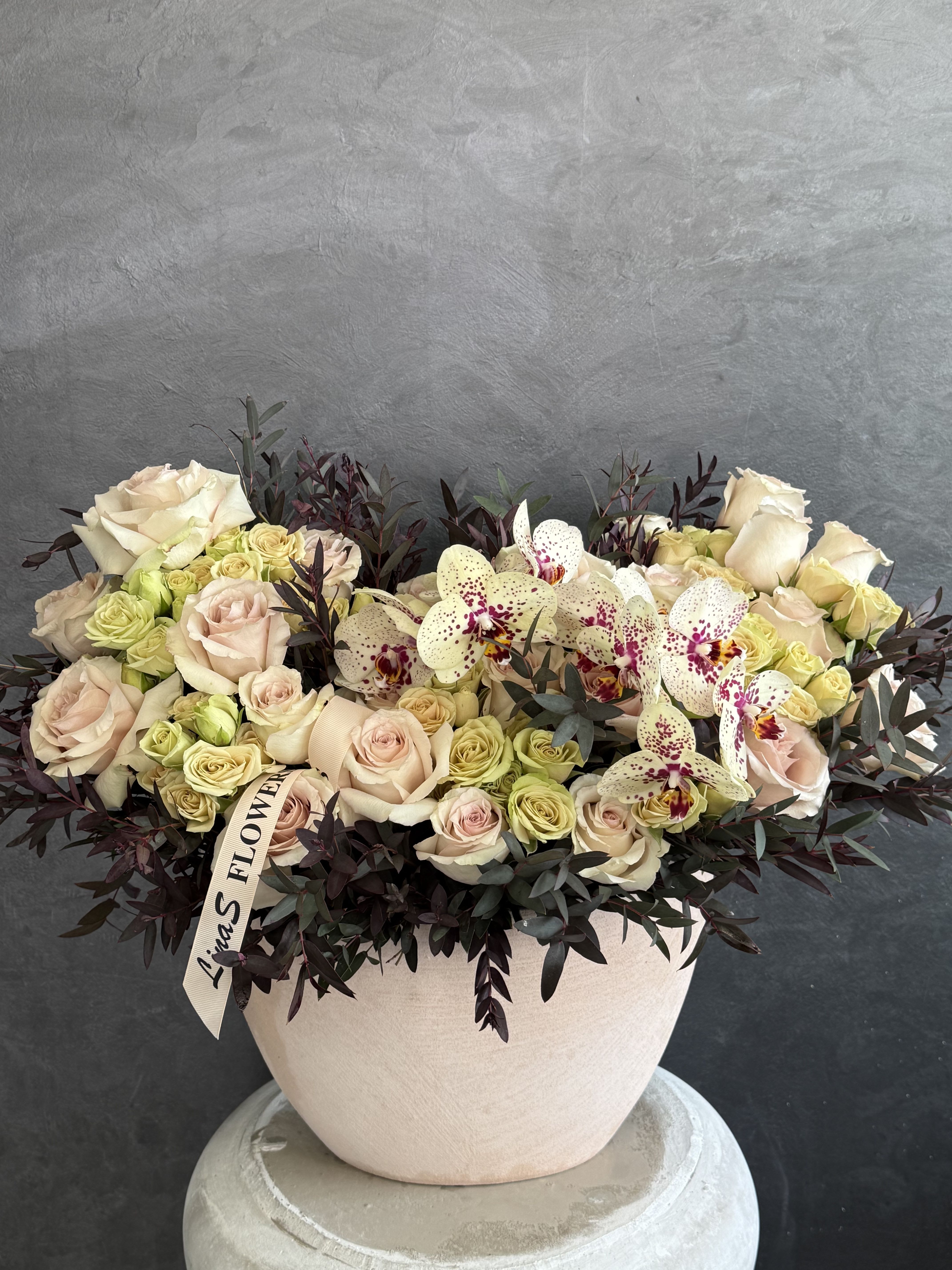 Cream roses and spotted orchids in a round blush vase