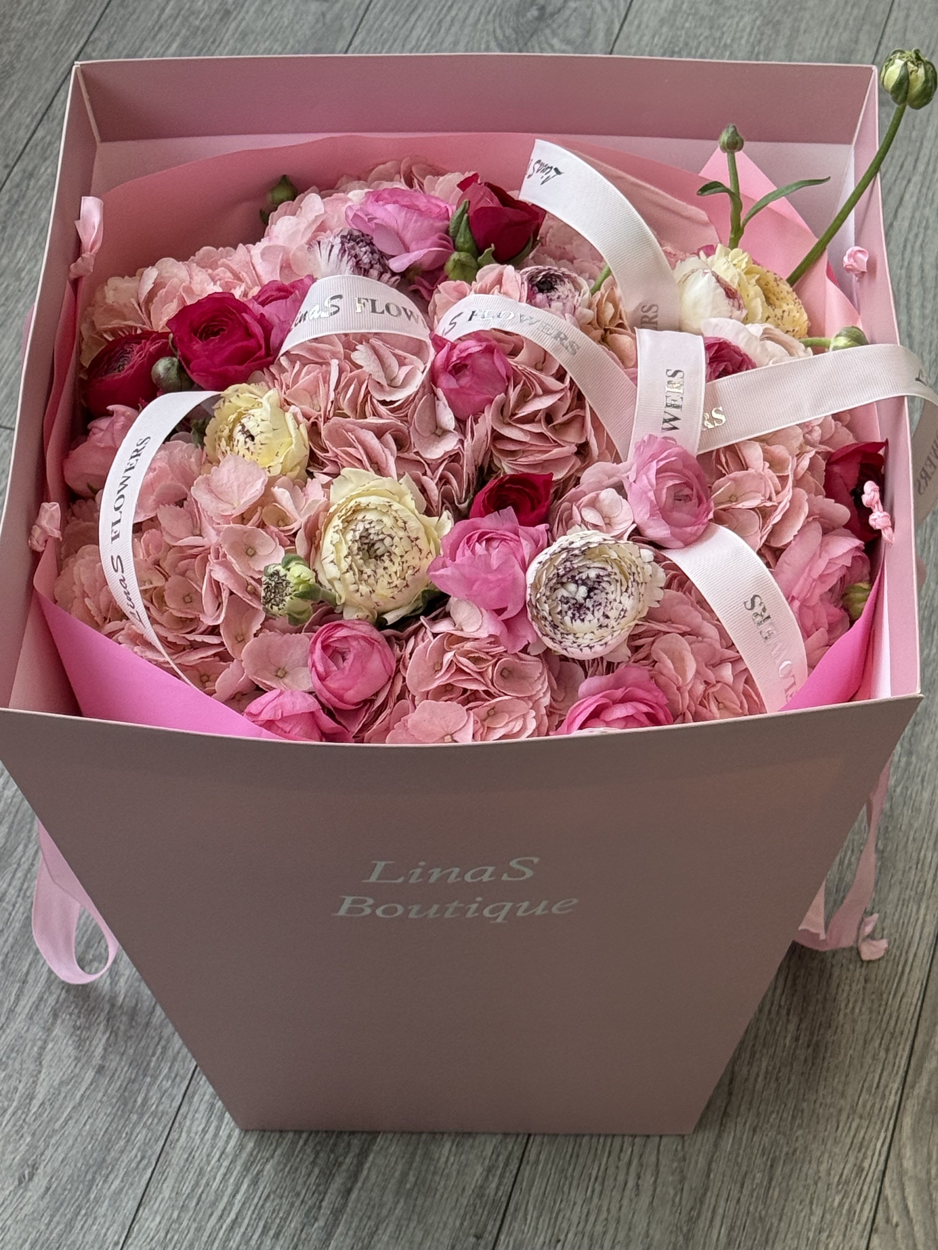 Pink bouquet in a box with roses and hydrangeas tied with white ribbons