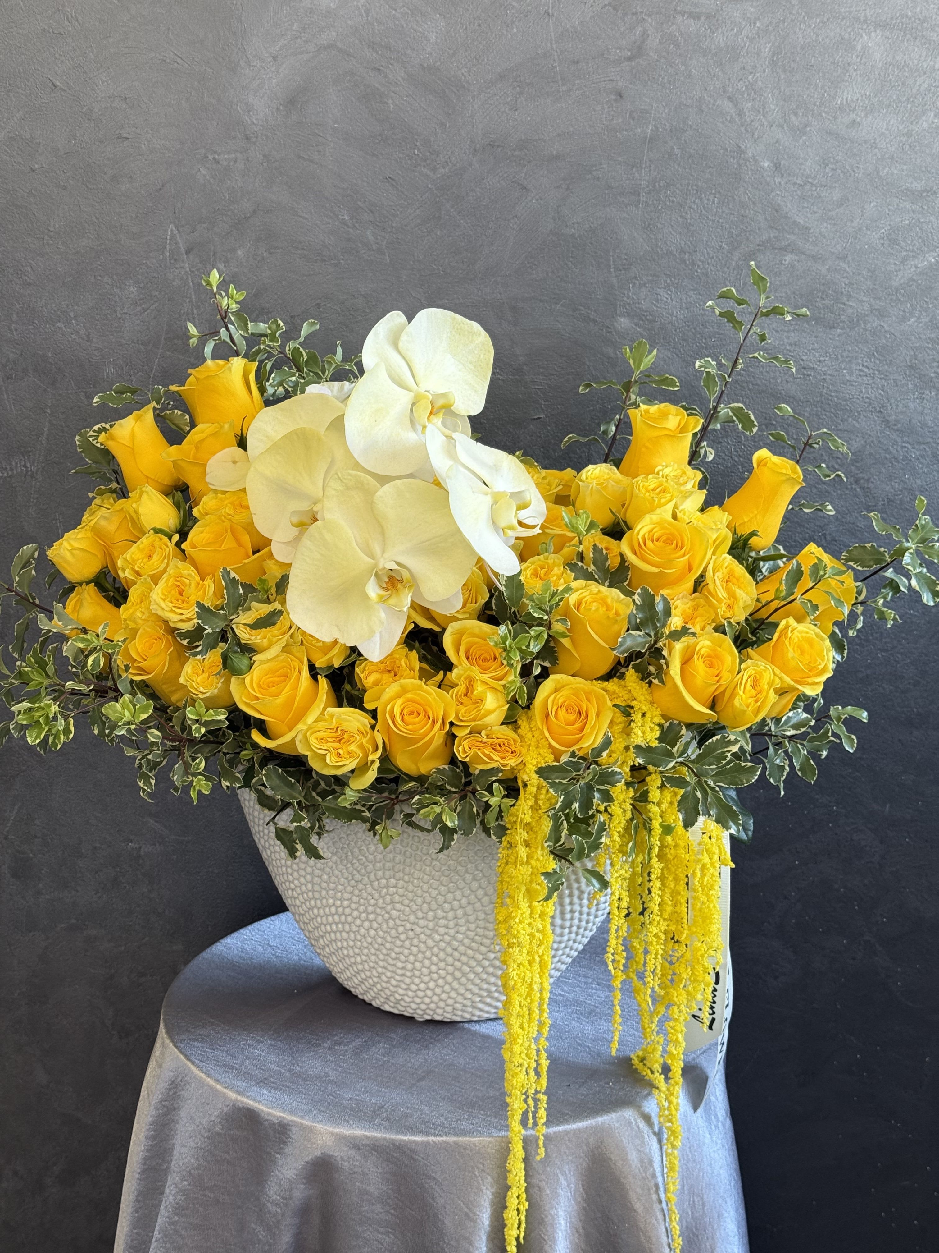 Yellow roses and white orchids in a textured white vase