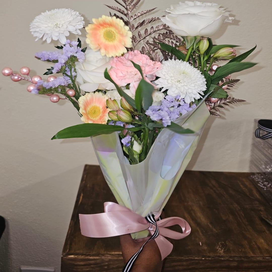 Bouquet of mixed pastel flowers wrapped in translucent paper with a pink ribbon