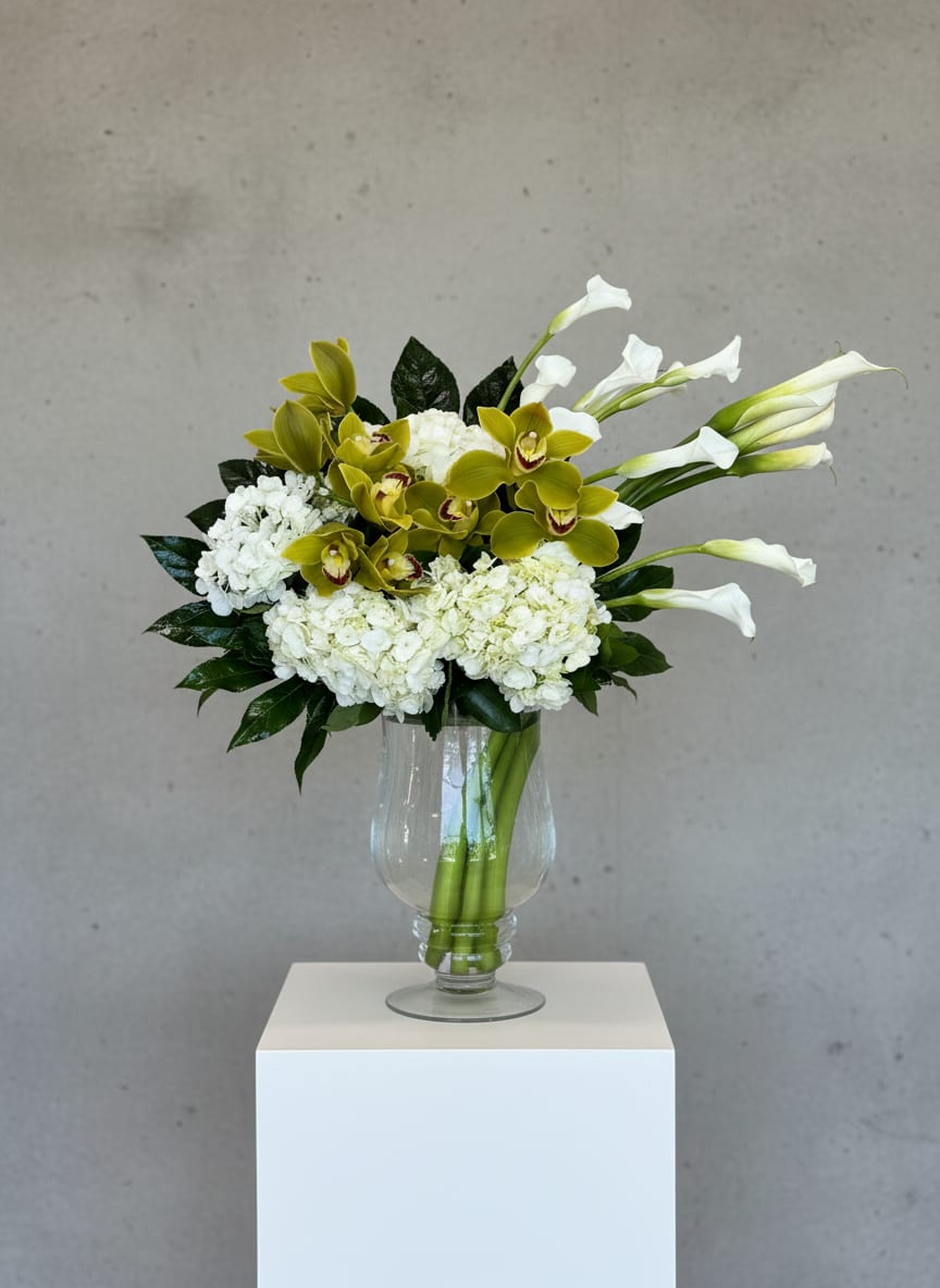 Modern Serenity - A refined expression of peace and elegance, this modern arrangement is designed with simplicity and intention. Featuring graceful calla lilies, lush hydrangeas, and striking cymbidium orchids, it showcases a harmonious blend of texture, form, and soft color.  The clean lines and minimalist composition create a calming presence, making it a beautiful choice for offering comfort, expressing sympathy, or bringing a sense of tranquility into any space.  Presented in a clear glass vase, this arrangement embodies understated luxury and timeless design, perfect for those who appreciate modern elegance and quiet beauty.