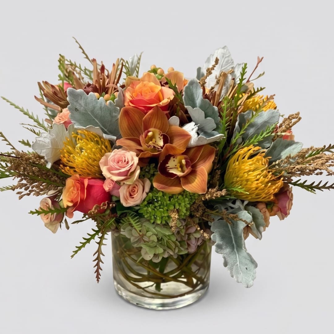Mixed bouquet of orange, pink, and yellow flowers in a clear glass vase