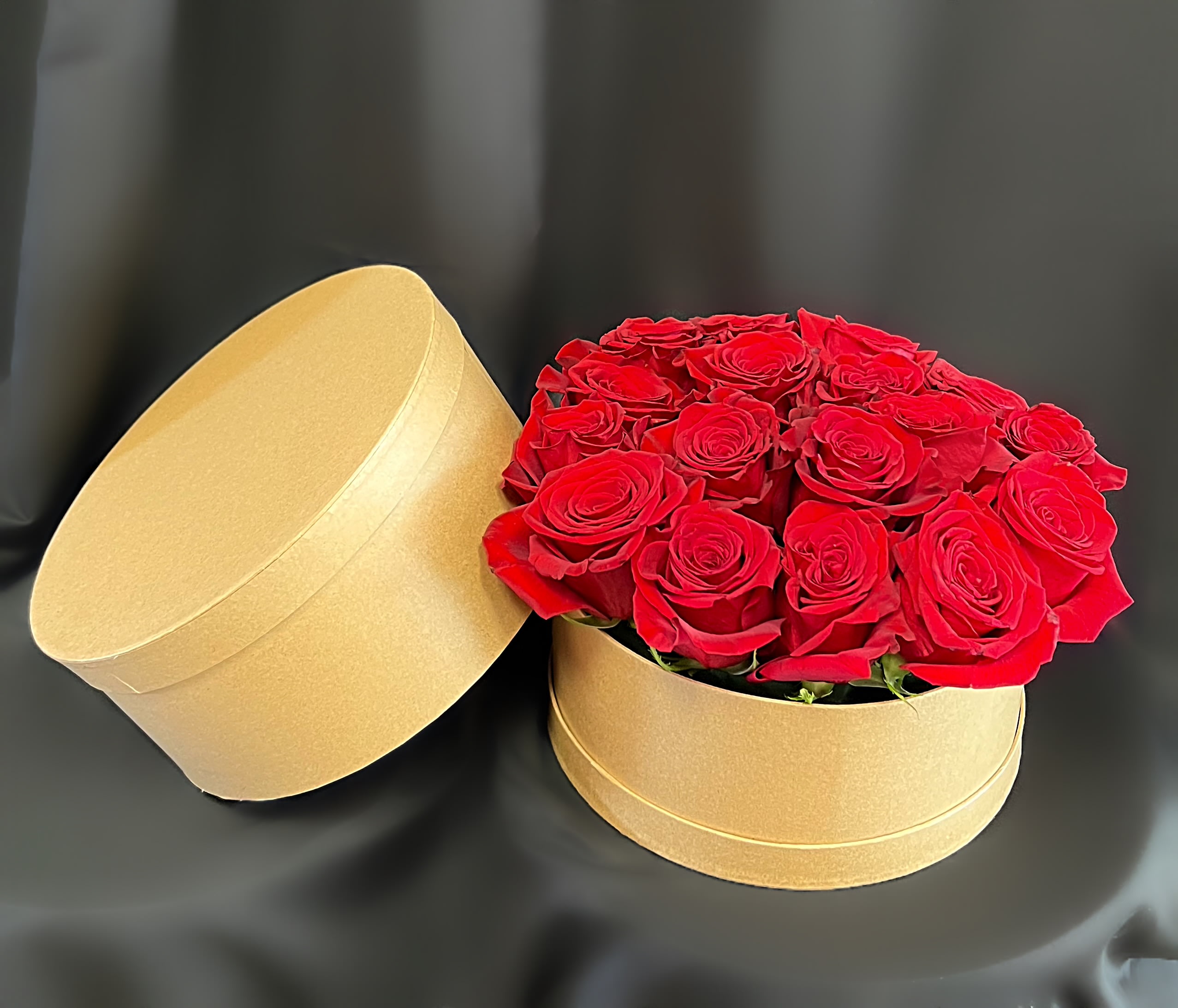 Red roses arranged in a round gold gift box with the lid beside it
