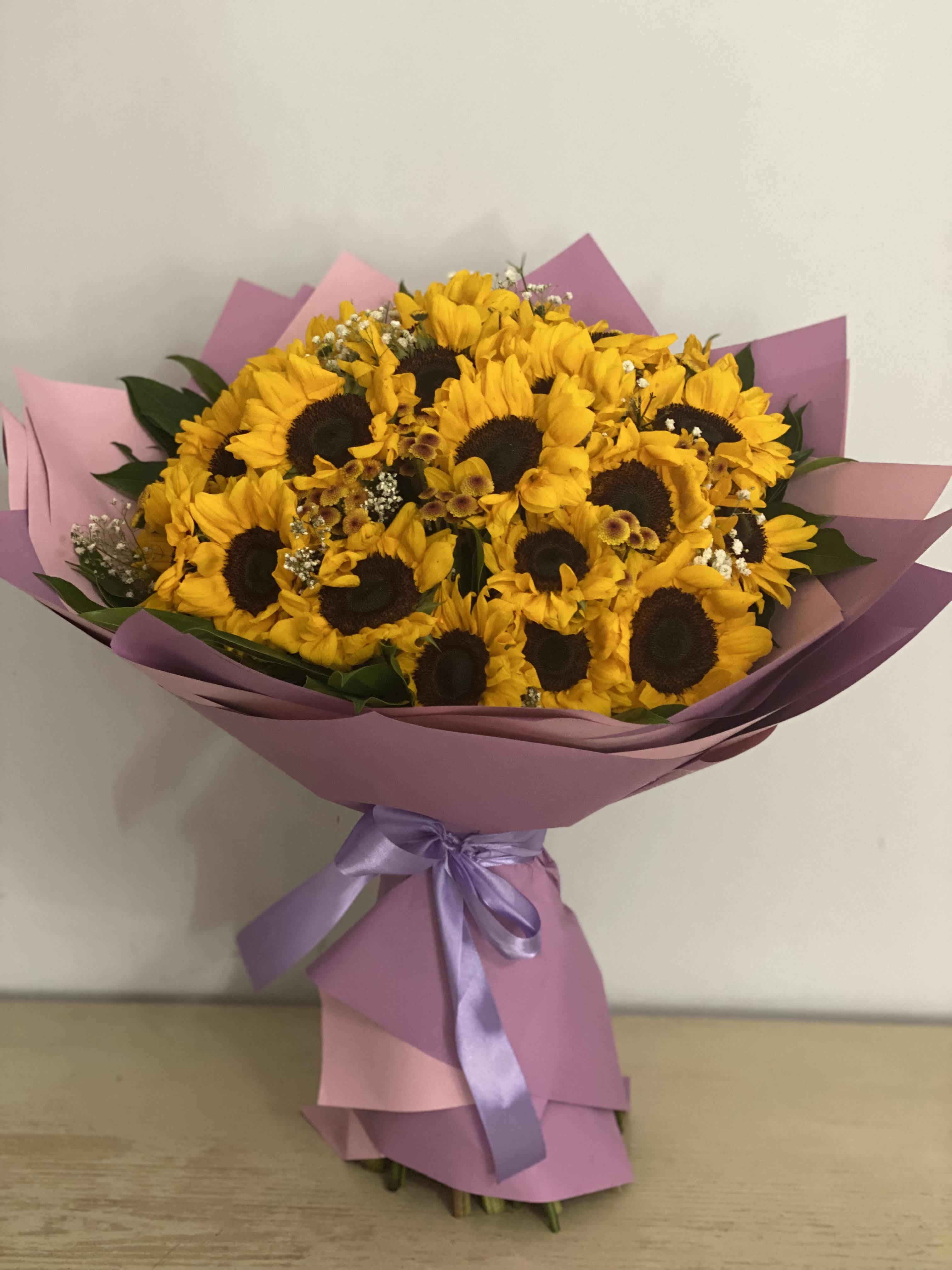Bouquet of yellow sunflowers wrapped in pink paper with a lavender ribbon