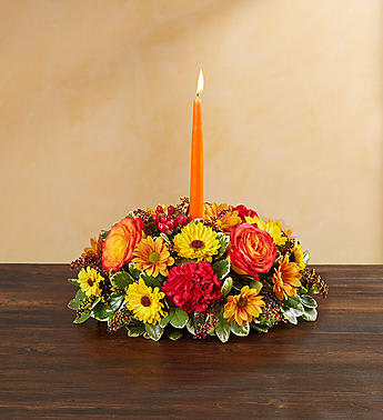 Low floral centerpiece with a lit orange taper candle in the middle