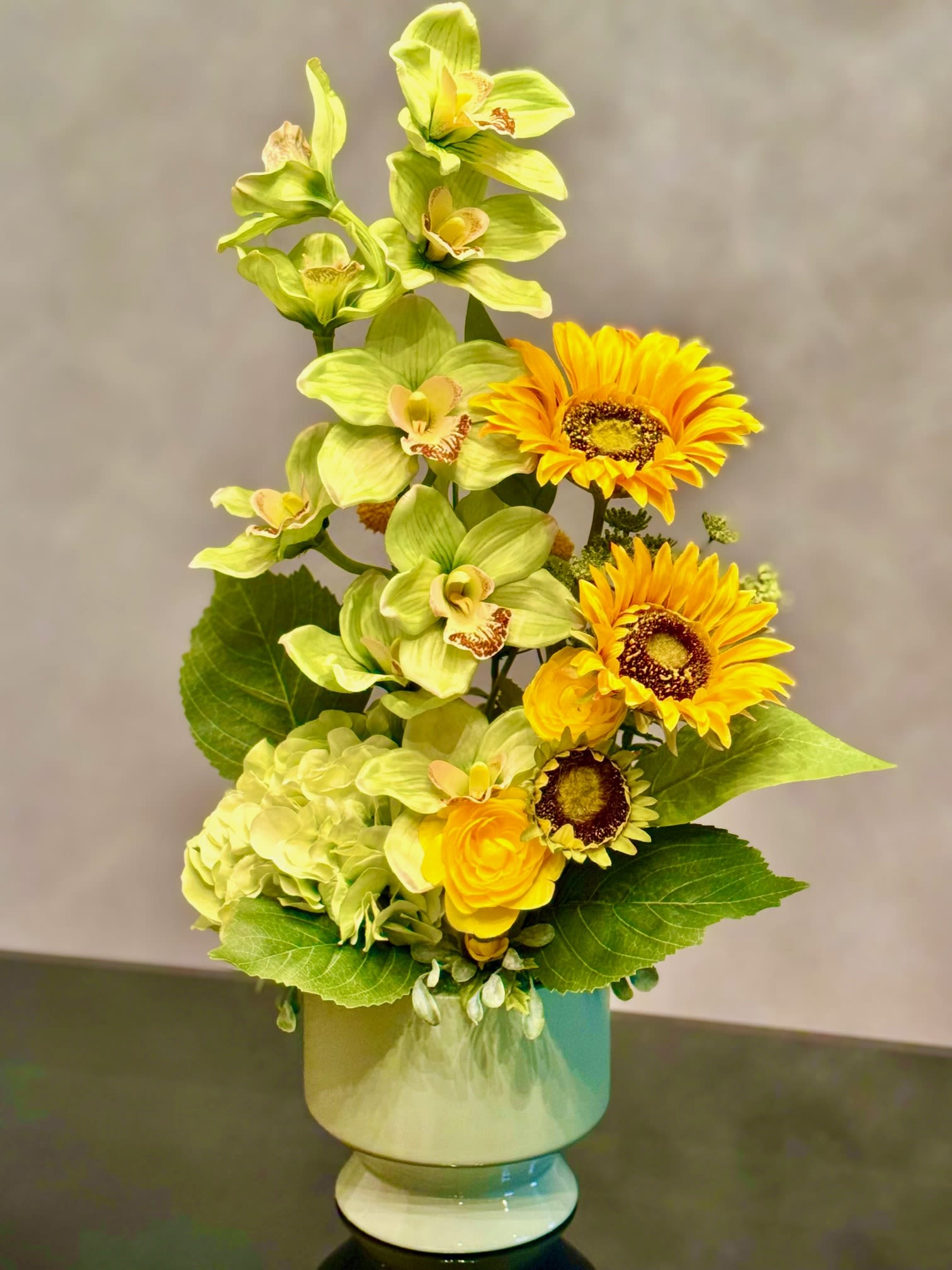 Yellow flowers and green orchids arranged in a pale vase