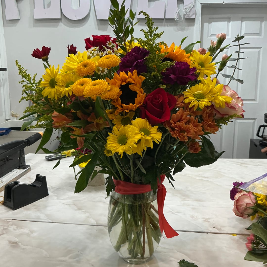 Mixed bouquet of yellow, red, purple, and orange flowers in a glass vase