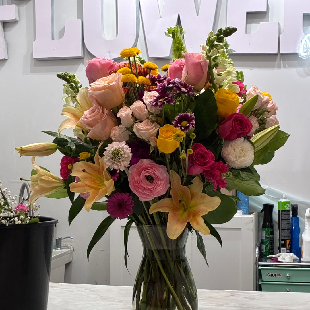 Mixed bouquet of pink, yellow, and white flowers in a clear glass vase
