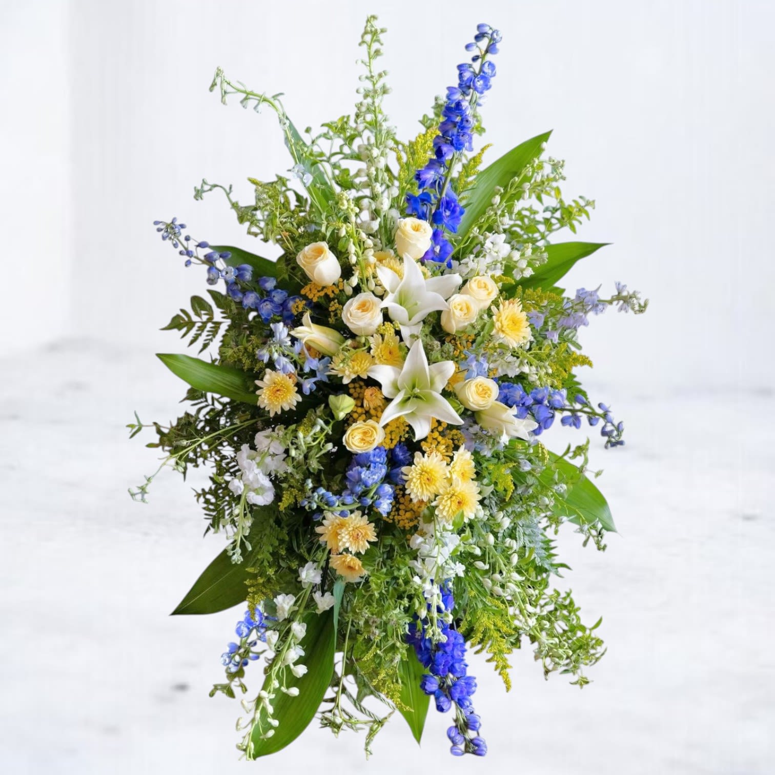 Tall floral spray with white lilies, cream roses, and blue flowers