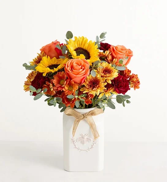 Bouquet of sunflowers, roses, and mums in a white vase with a ribbon